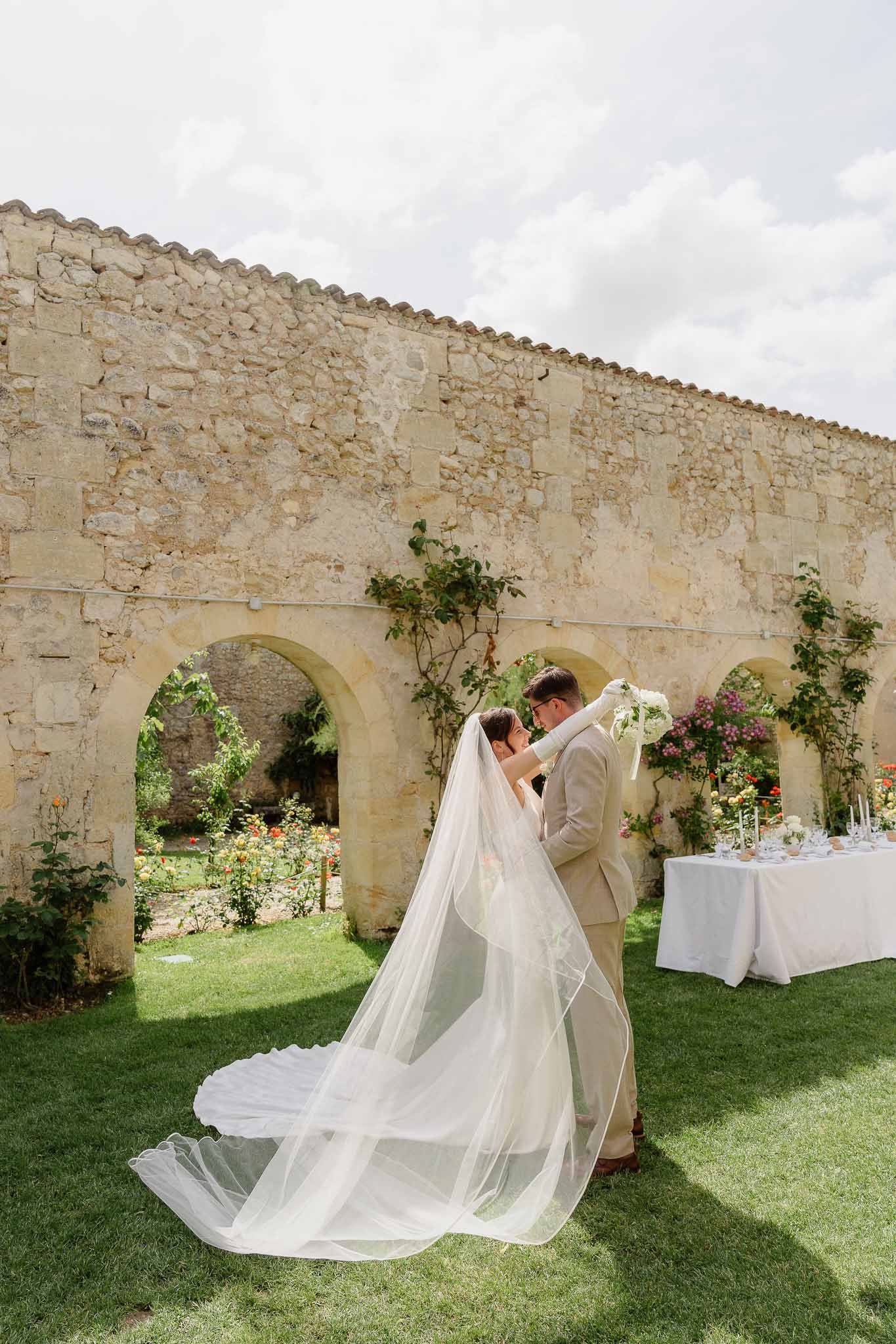 Couple leaning heads together in stone courtyard with cathedral-length veil spread across lawn