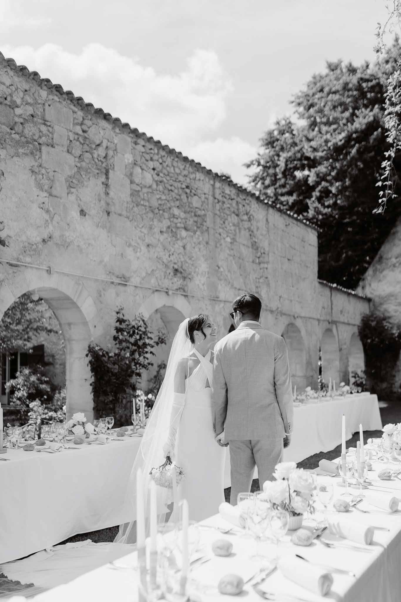 Black and white couple walking between reception tables, bride in cross-back gown with cathedral veil