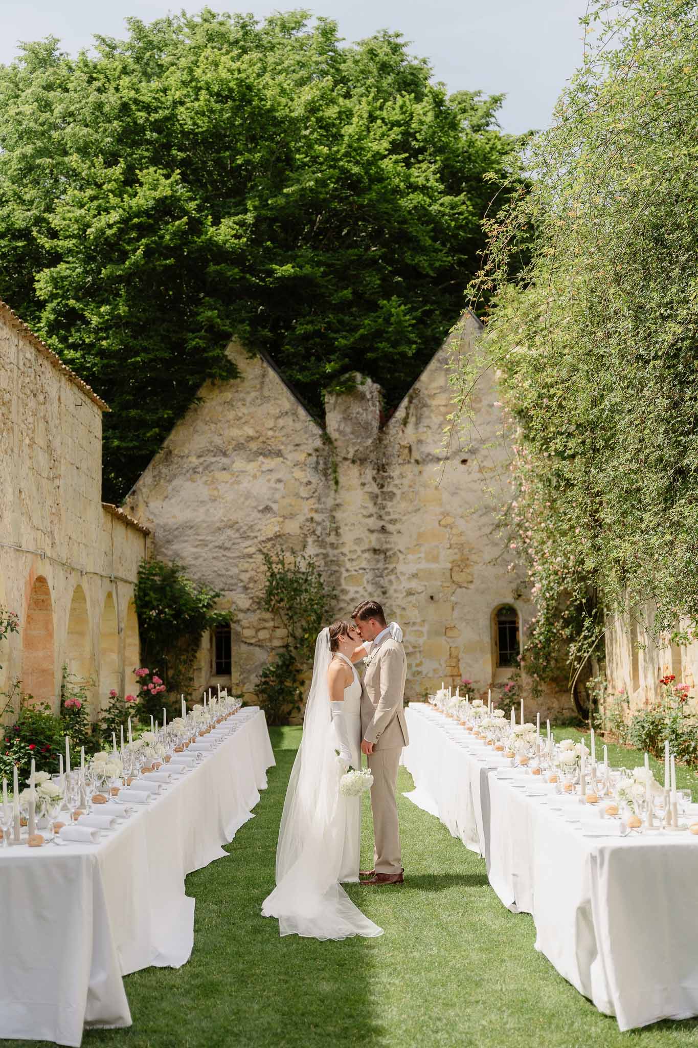 Bride and groom touching foreheads between two banquet tables set with white linens in stone courtyard