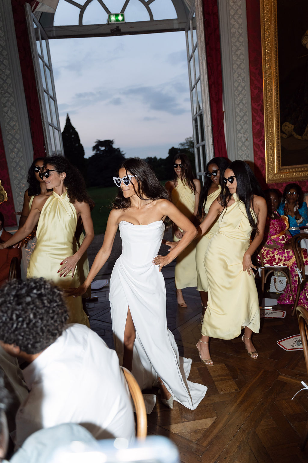 Bride and four bridesmaids in yellow satin dresses performing choreographed entrance in red damask chateau ballroom