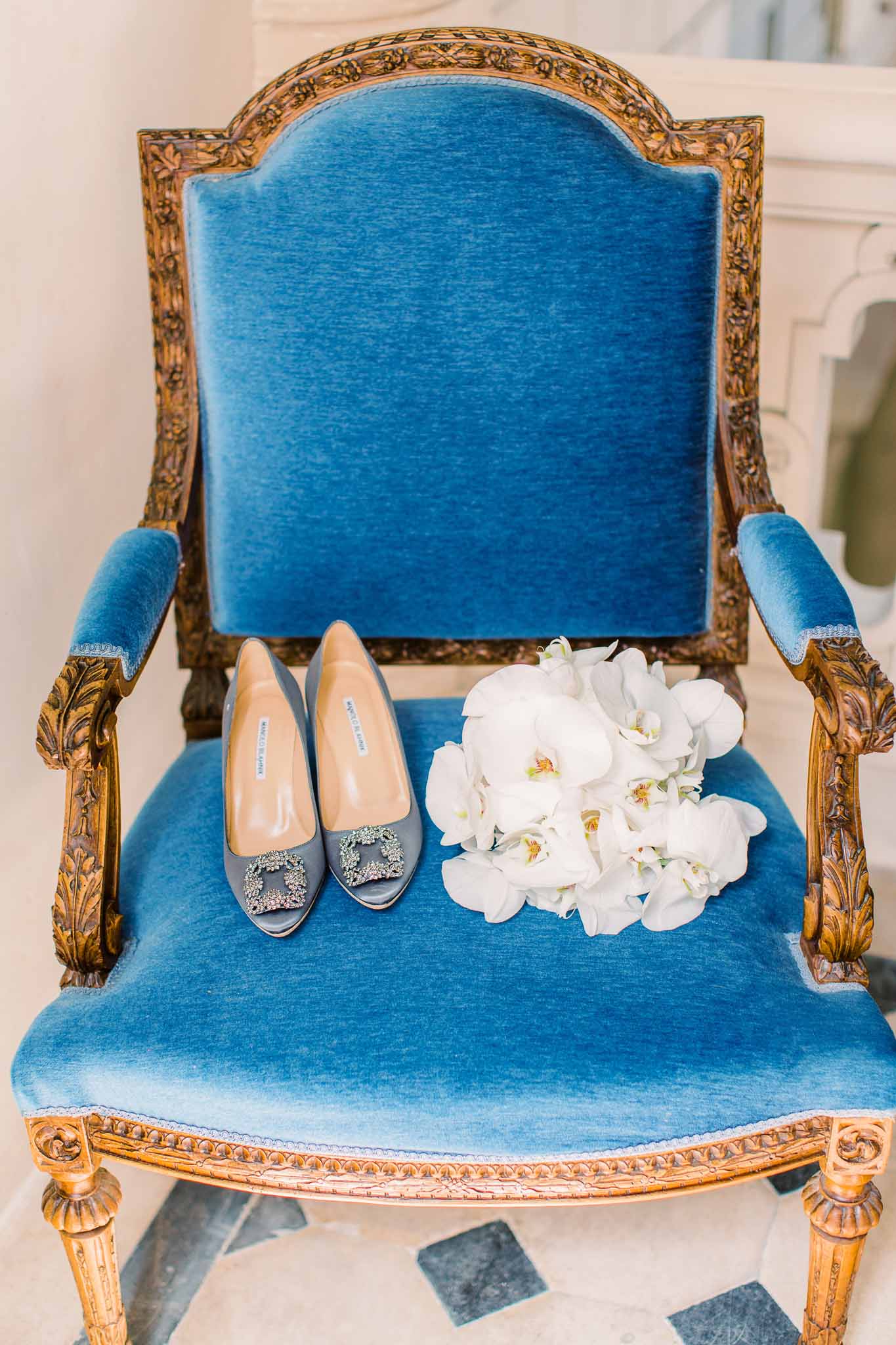 Manolo Blahnik slate-blue Hangisi heels with white orchid bouquet on gilt armchair in cobalt velvet