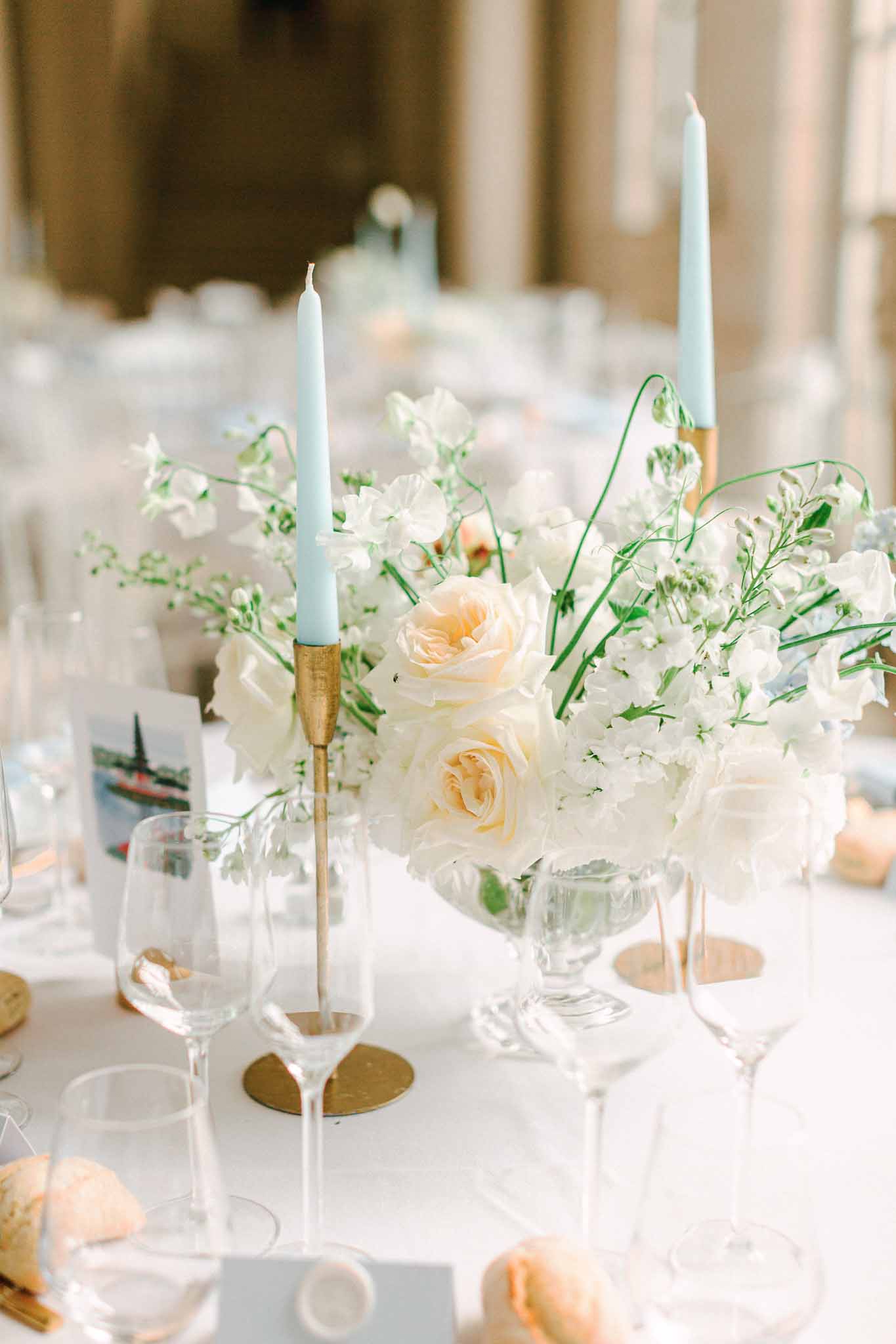 Reception centerpiece with blush roses and white sweet peas in glass compote, flanked by pale blue taper candles