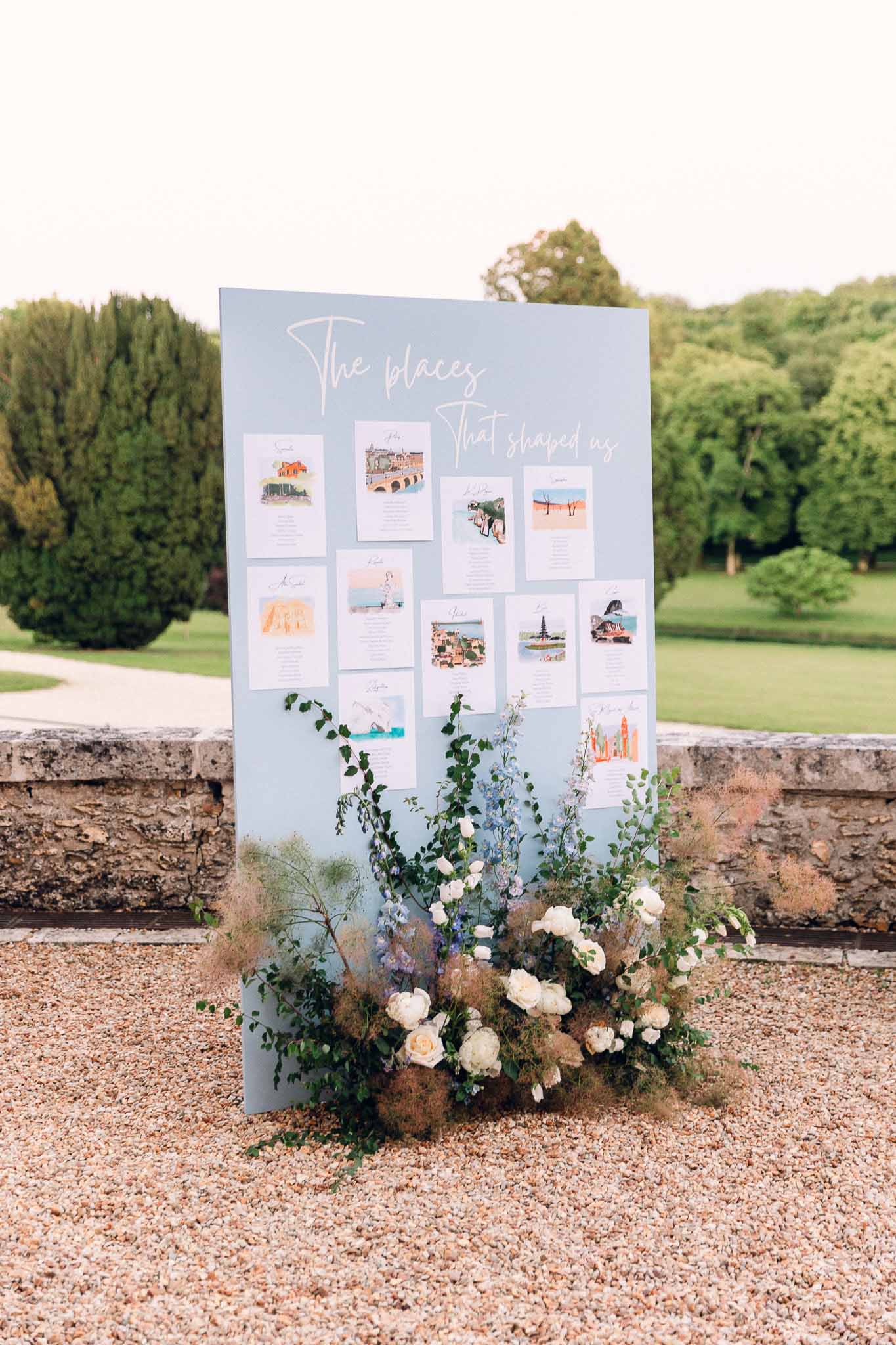 Travel-themed seating chart with watercolor destination illustrations and white and blue floral arrangement