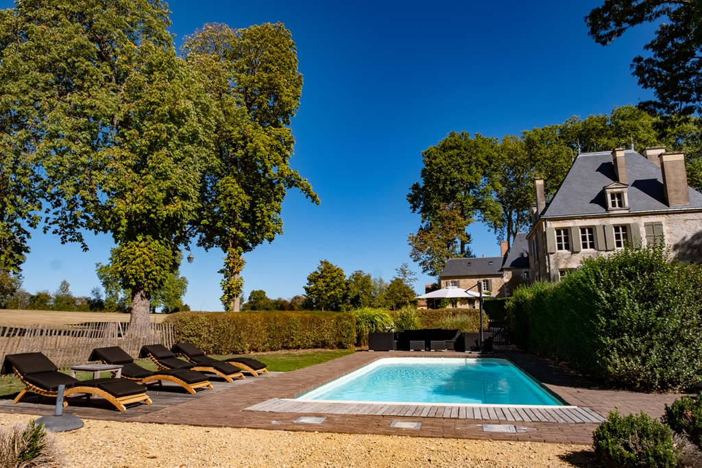 French manor with swimming pool on wooden deck, sun loungers, and slate mansard roof