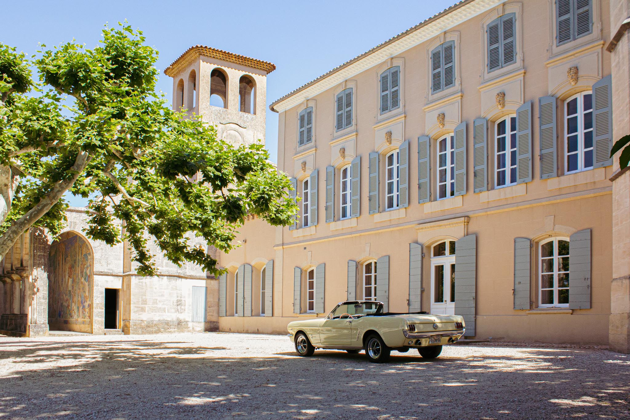 Cream vintage Ford Mustang convertible parked in courtyard of a French manor house with stone chapel and bell tower