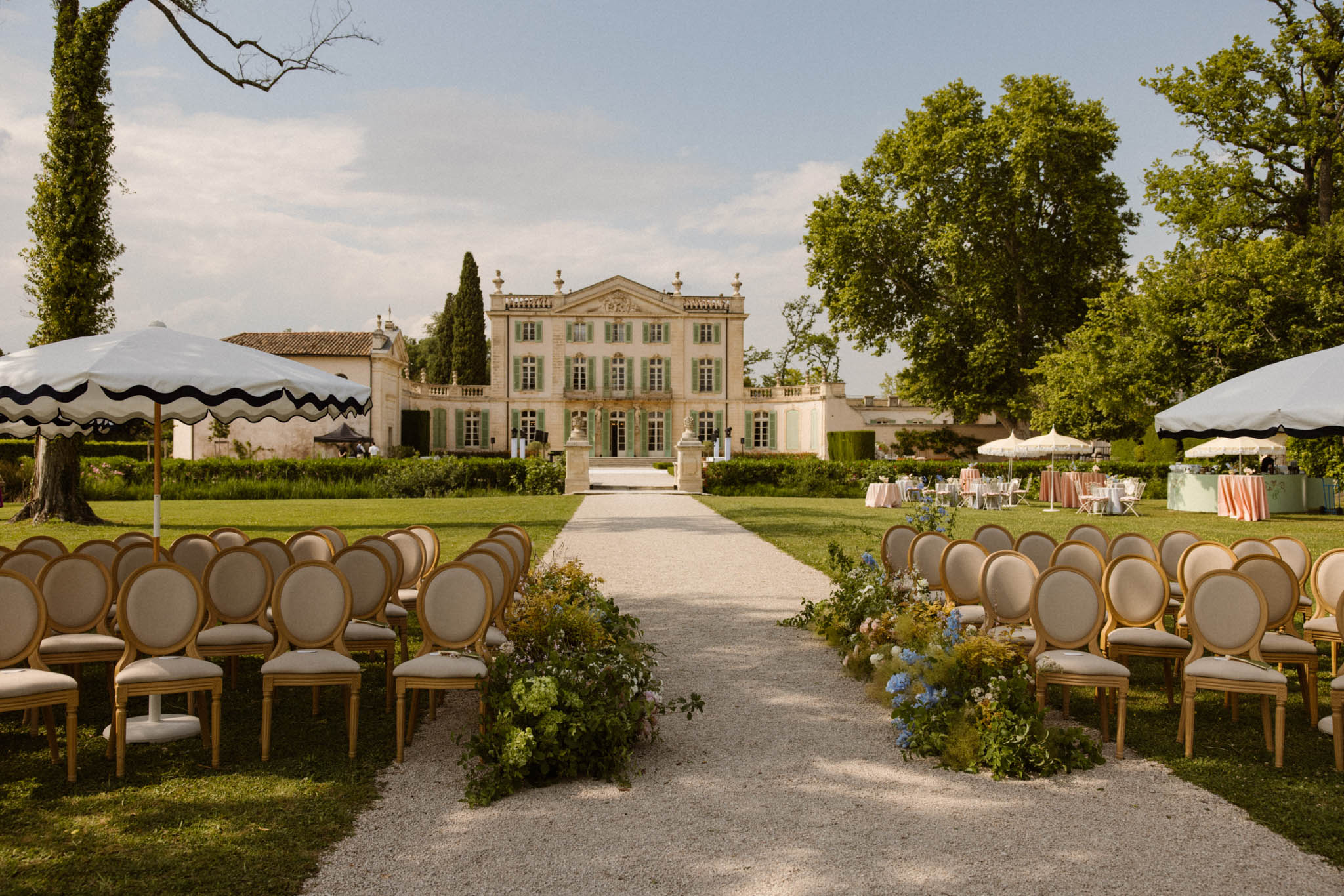 Ceremony setup with gold Louis chairs blue hydrangea aisle markers and chateau with sage shutters behind
