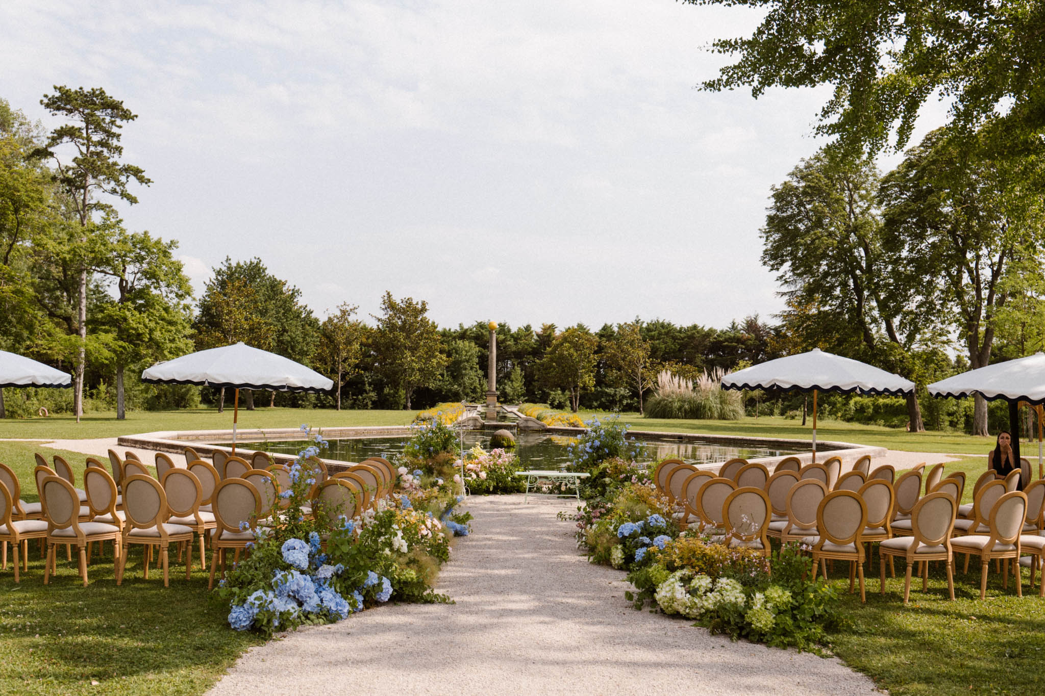 Gold Louis XVI chairs and blue hydrangea aisle before ornamental pond altar with white parasols