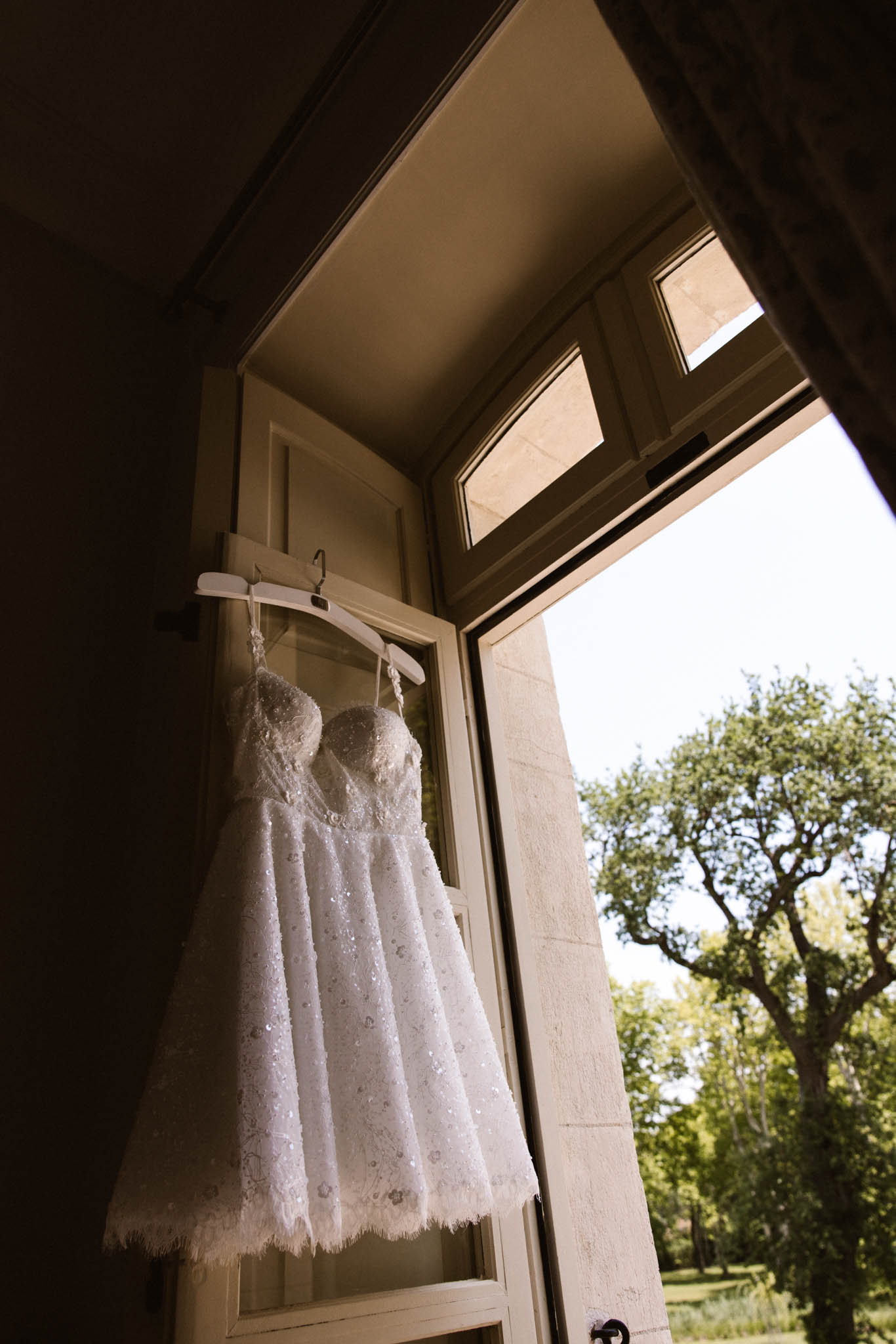 Beaded and embellished short white wedding dress hanging in a doorframe backlit by natural light