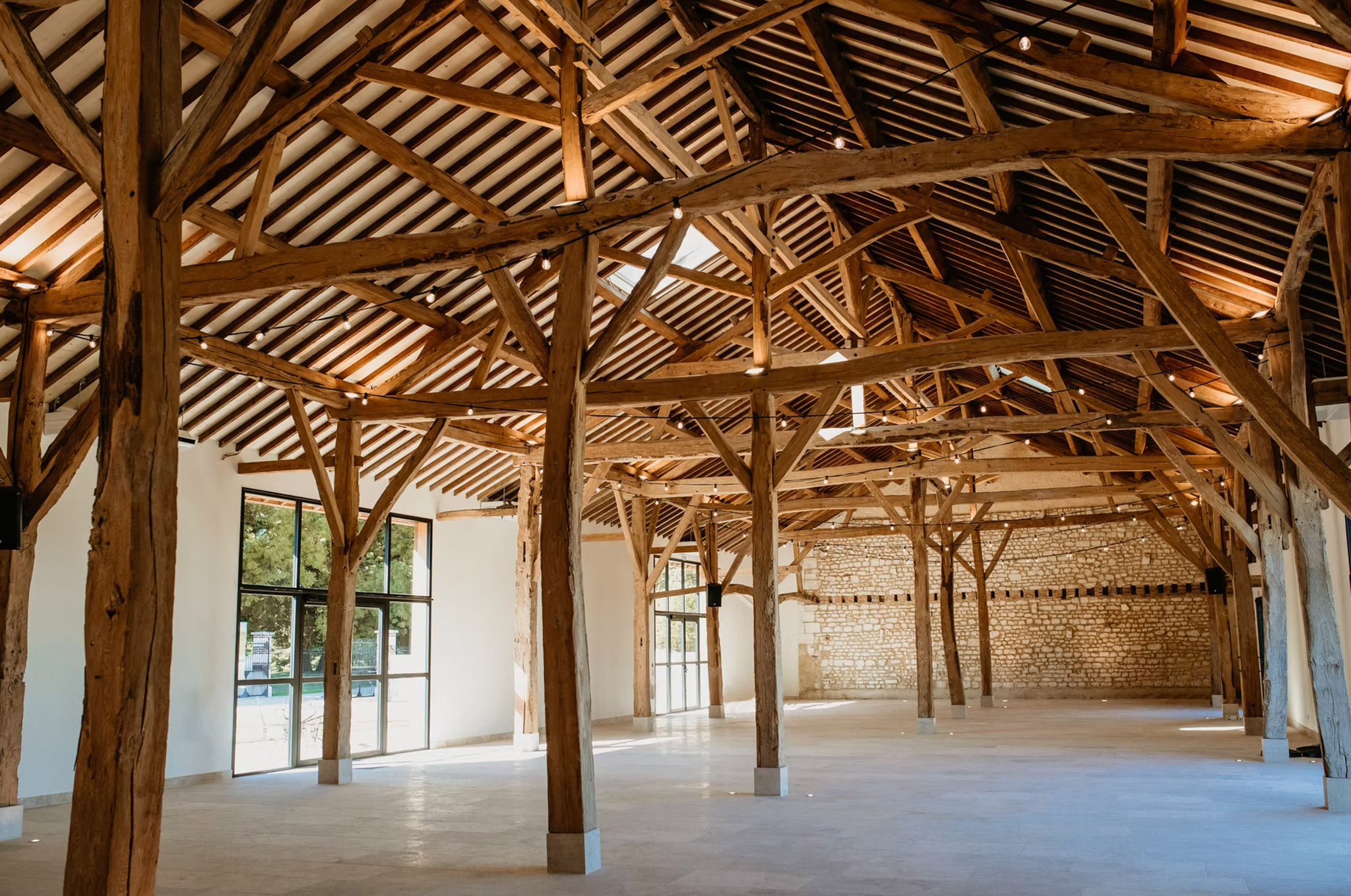 Converted barn interior with honey-toned timber trusses, stone wall, and industrial windows