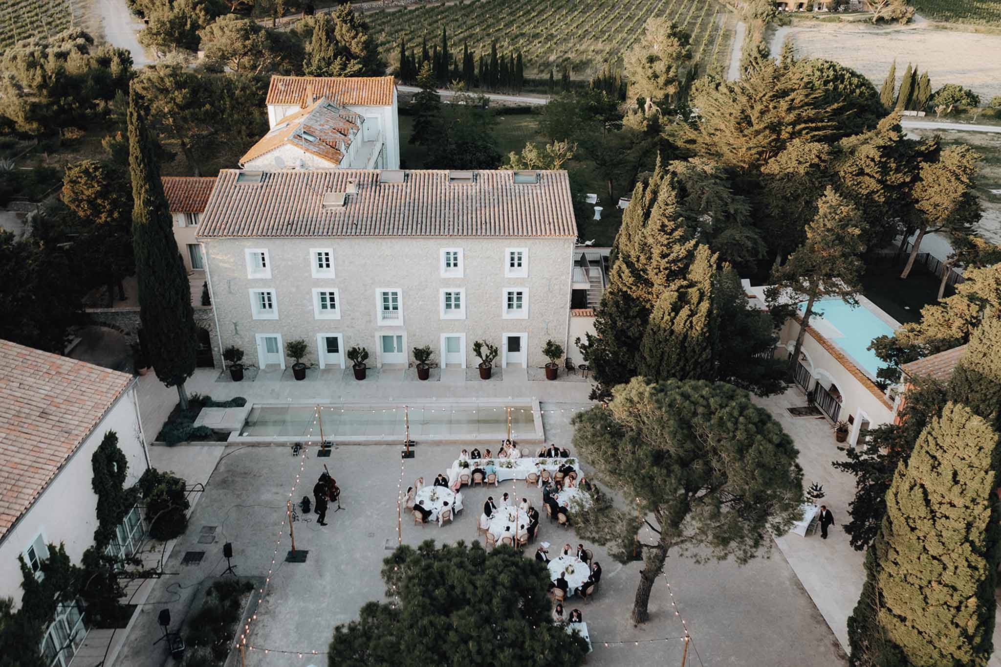 Aerial drone view of outdoor wedding reception in Provencal mas courtyard with round tables and fairy lights at dusk