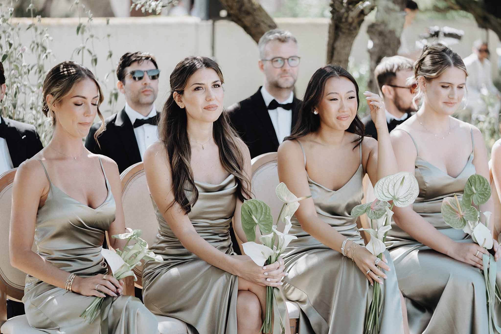 Four bridesmaids in sage green satin dresses holding white calla lily bouquets during ceremony