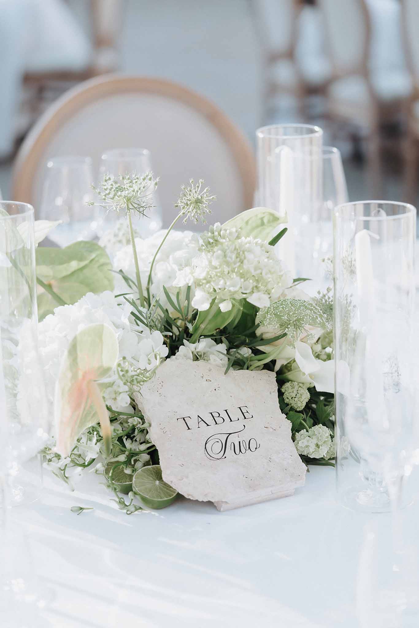 White hydrangea and green anthurium centerpiece with stone table number and hurricane vases on white linen