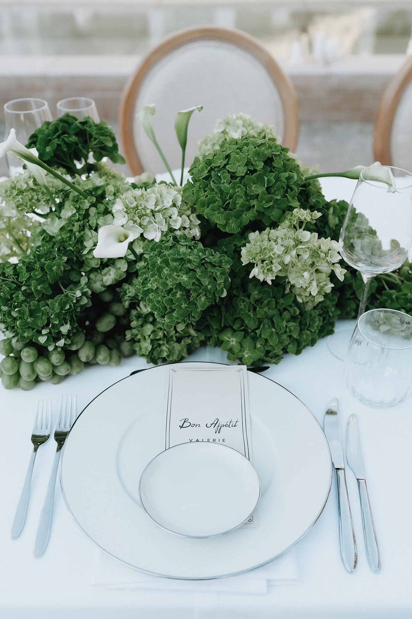 Place setting with Bon Appetit menu card beside green hydrangea and white calla lily centerpiece