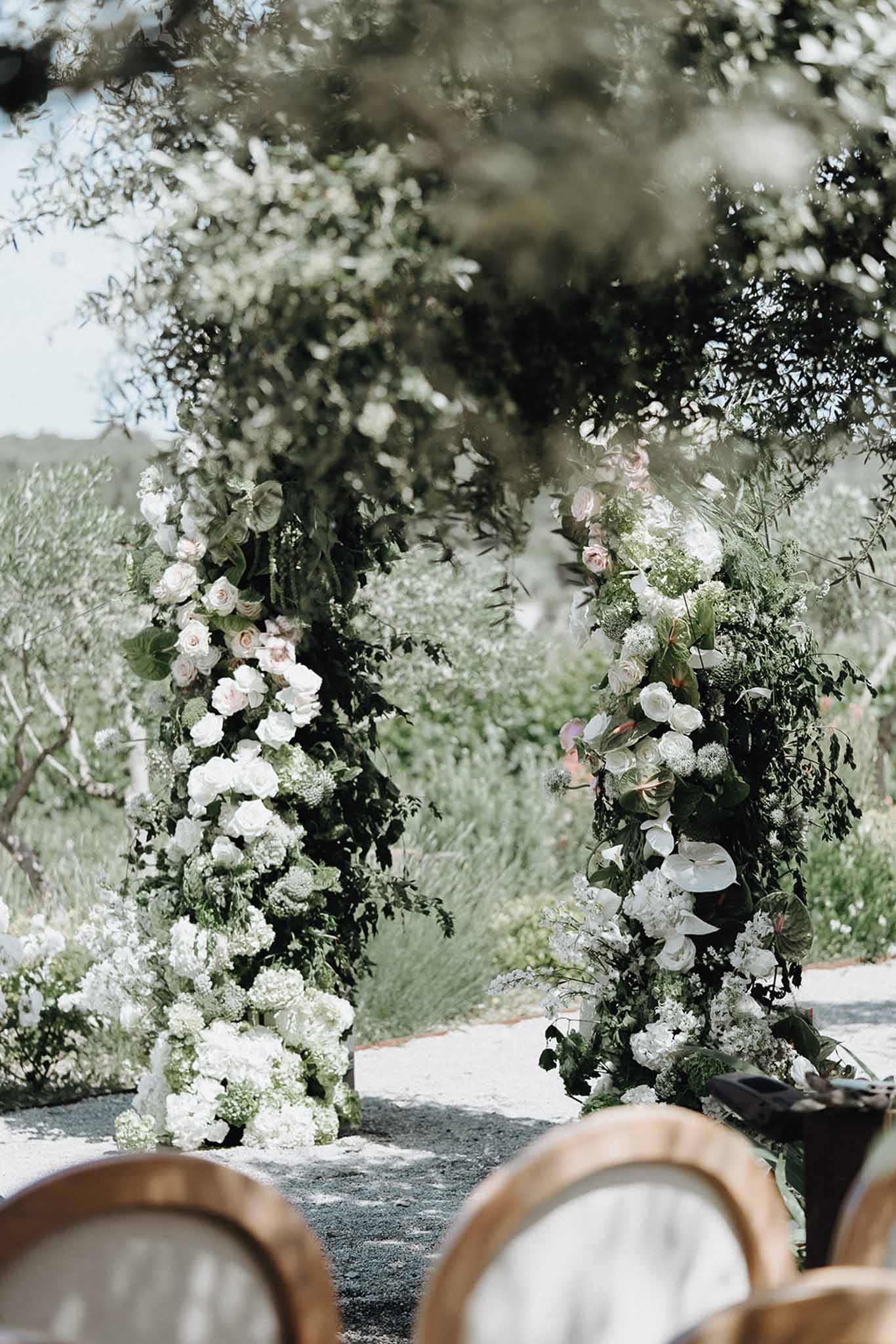 Two floral column arrangements of white hydrangeas, blush roses, and trailing greenery forming ceremony arch