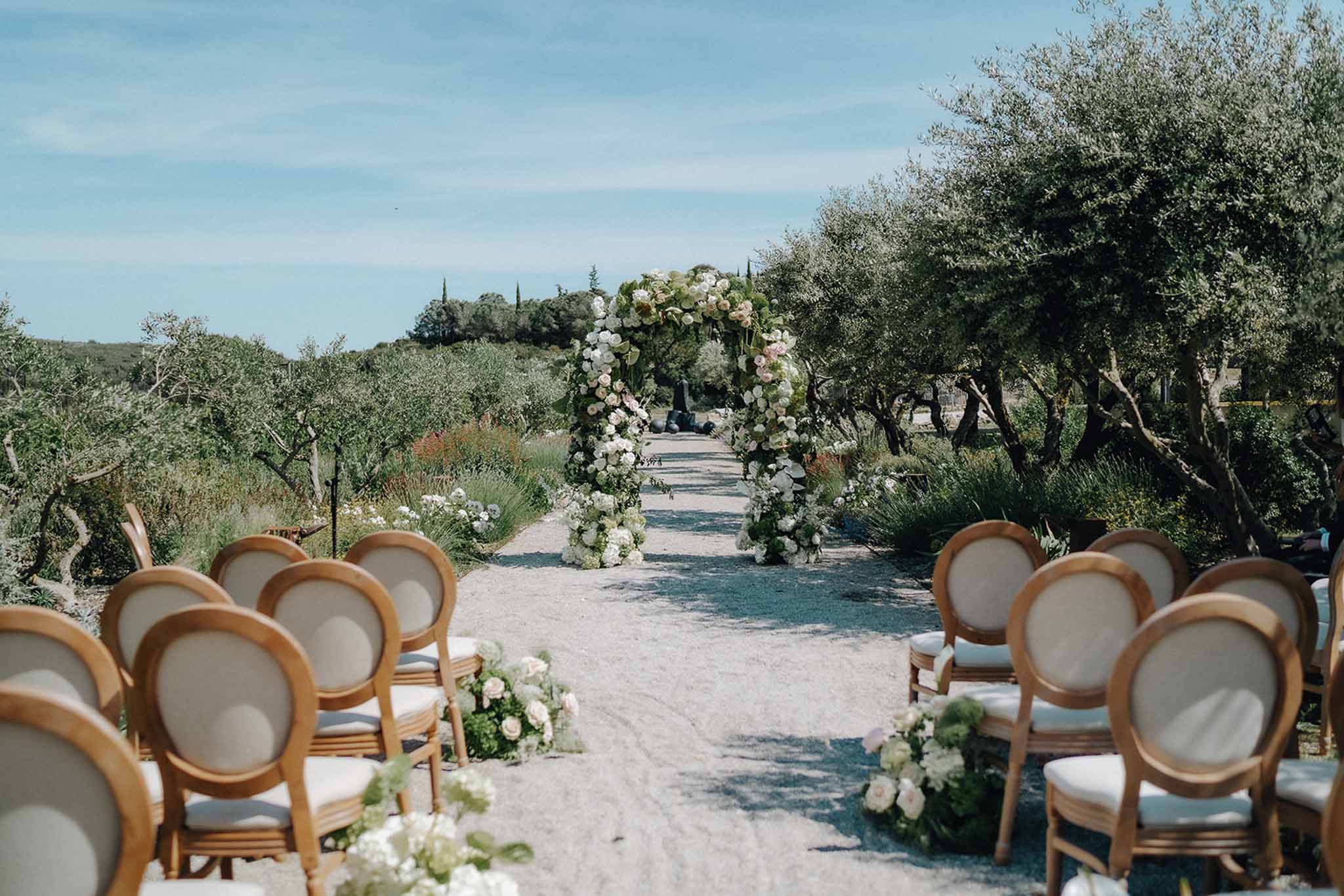 Ceremony aisle with Louis XVI chairs and circular blush and white rose arch on gravel path