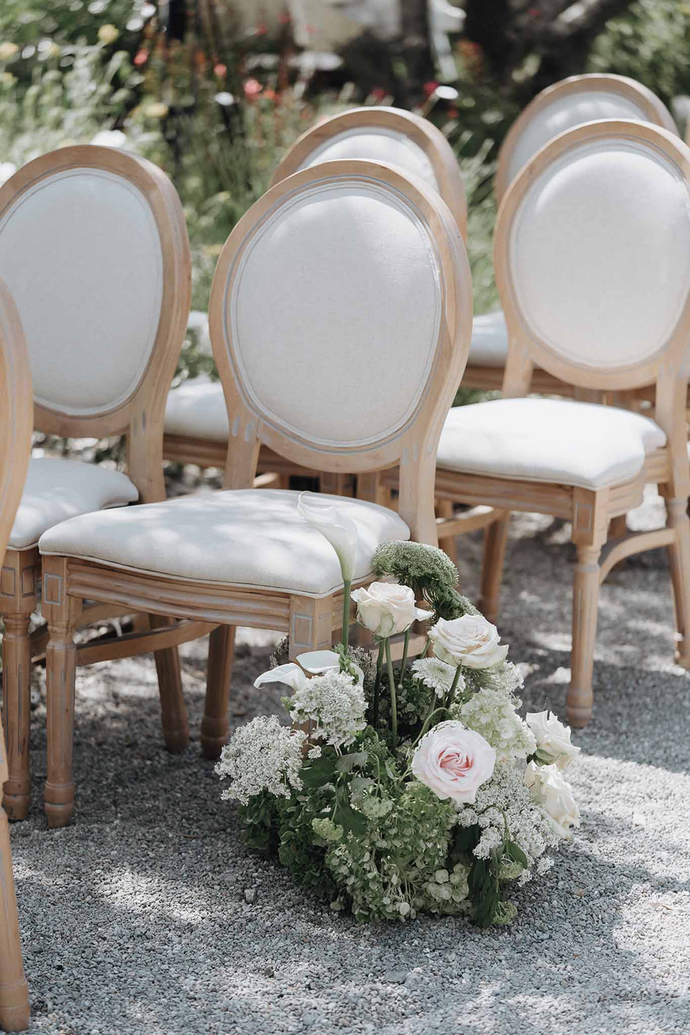 Outdoor ceremony aisle with Louis XVI chairs and low blush and ivory rose arrangement on gravel at a French venue
