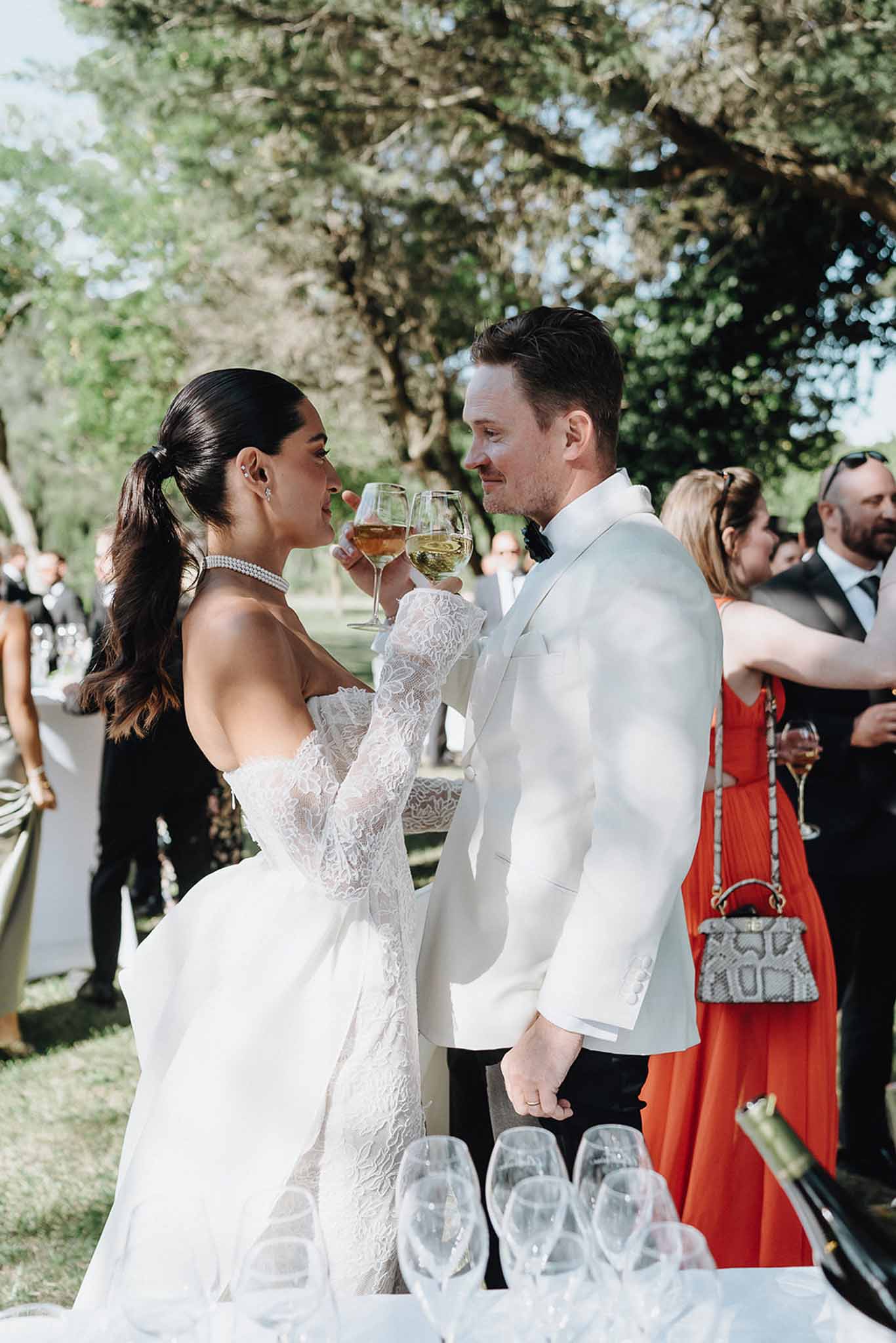 Couple clinking wine glasses at cocktail hour bride in strapless gown with pearl choker groom in white dinner jacket