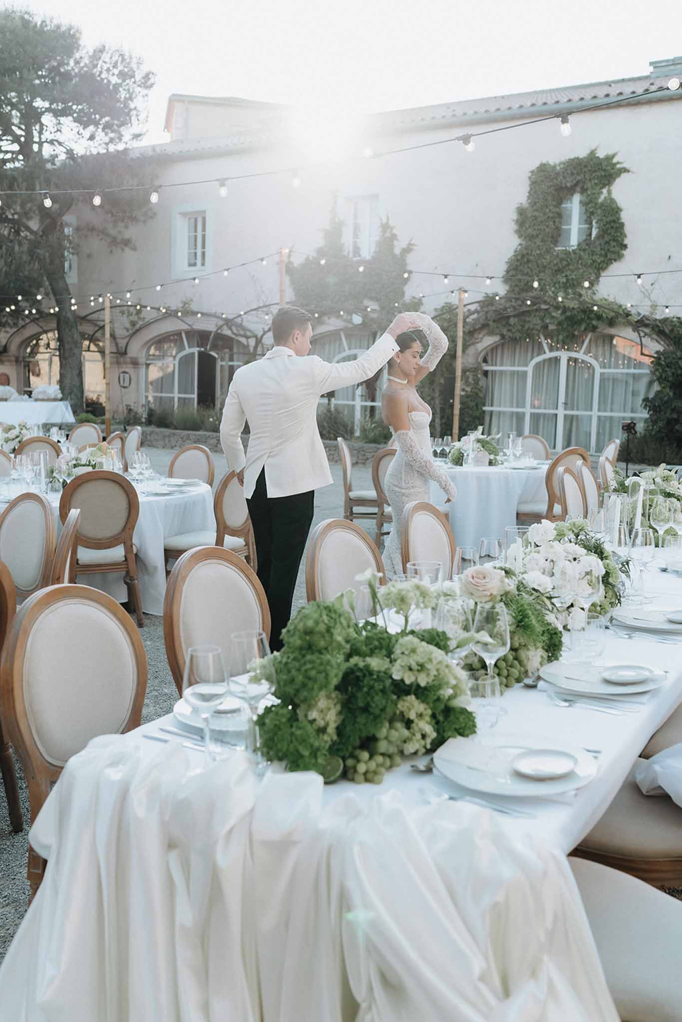 Couple dancing among set reception tables with green hydrangea centerpieces globe lights groom lifting brides cathedral veil