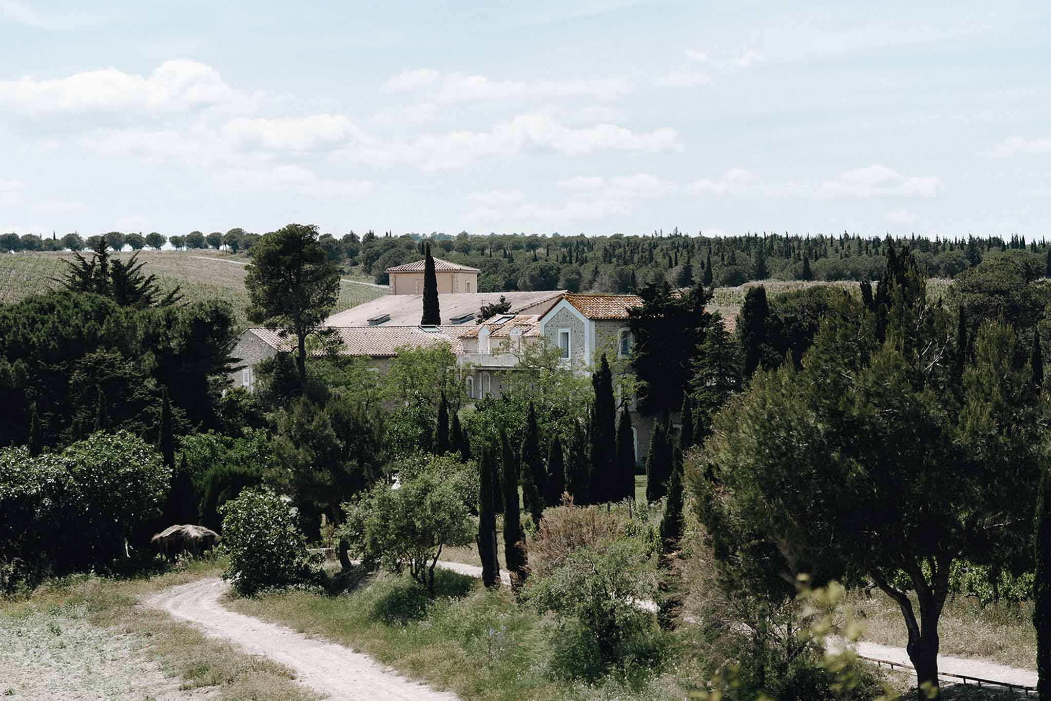 Aerial view of French country estate with stone buildings and terracotta roofs surrounded by cypress trees and vineyards