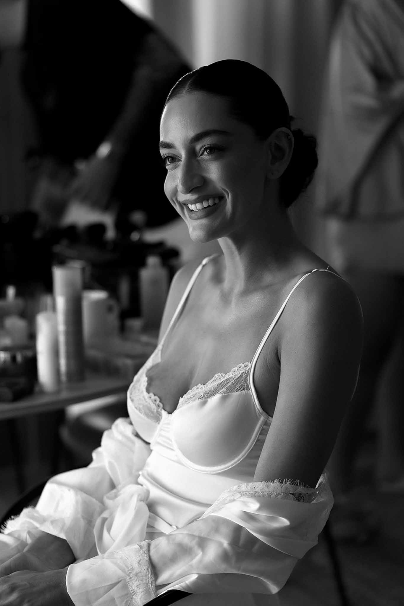 Black and white portrait of smiling bride in lace bridal lingerie and satin robe during getting ready