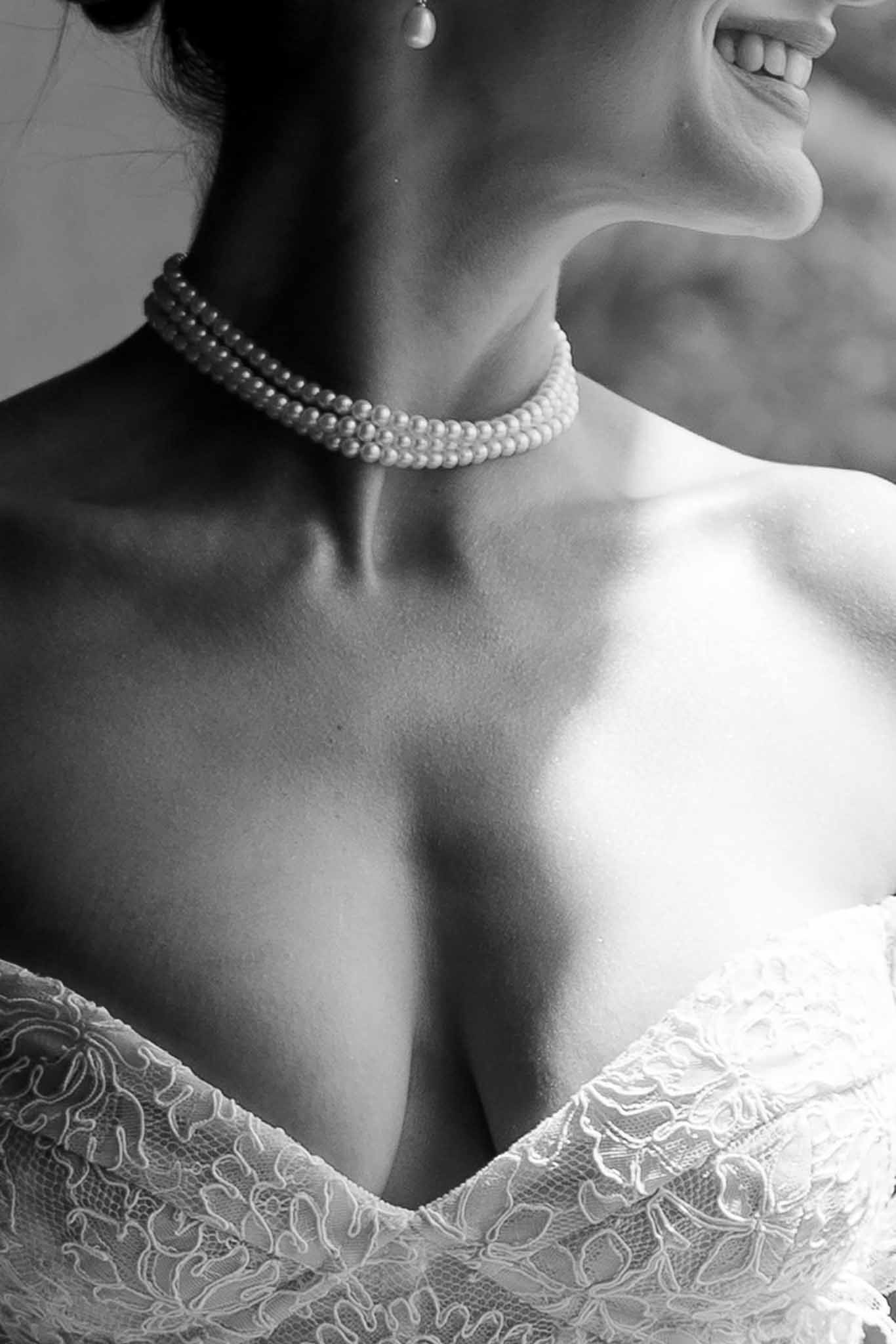 Black and white close-up of bride's pearl choker necklace and lace gown V-neckline