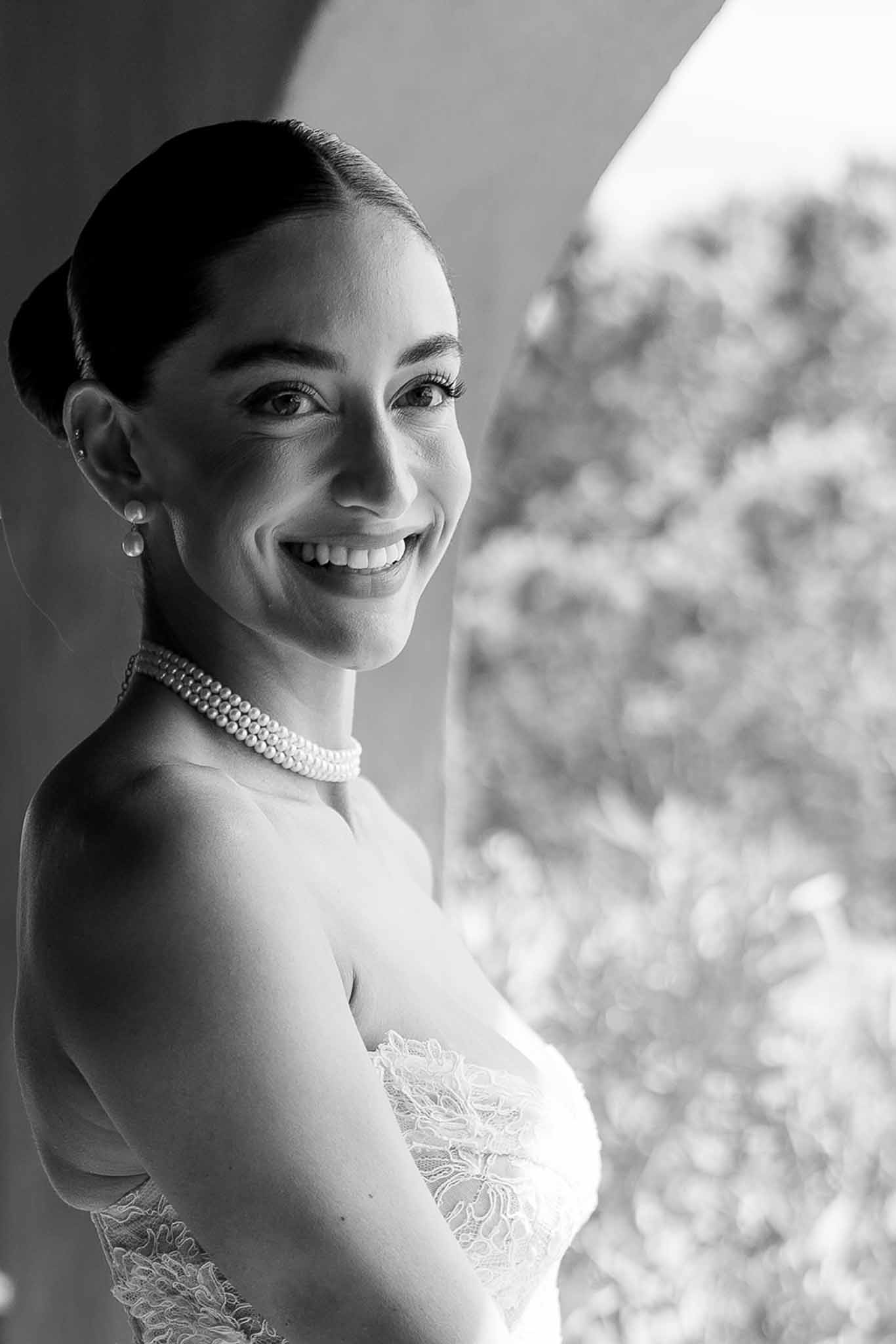 Close-up of smiling bride in strapless lace gown with pearl choker and sleek bun in black and white