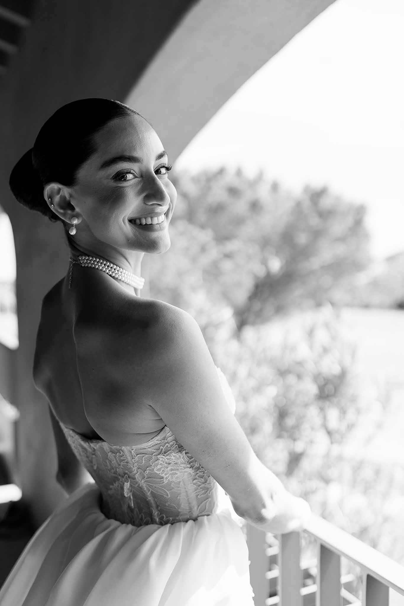 Black and white bridal portrait of bride on balcony in strapless lace gown with pearl choker and sleek low bun