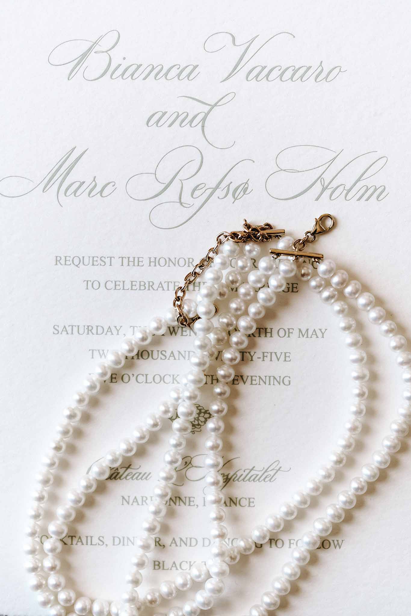 Wedding invitation in sage calligraphy with pearl bracelets and gold clasps on white card stock