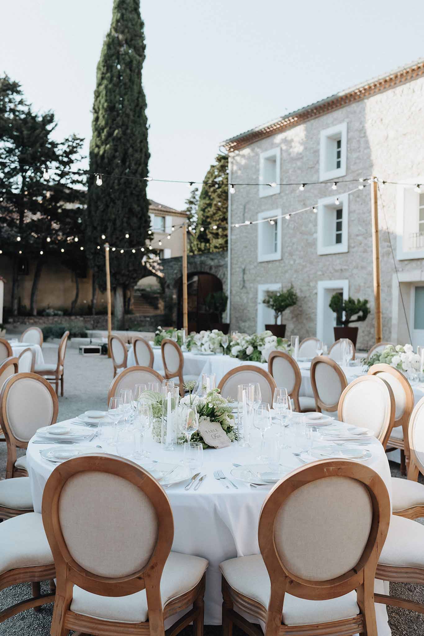 Outdoor courtyard reception at dusk with round tables, festoon lights, and white-green floral centrepieces