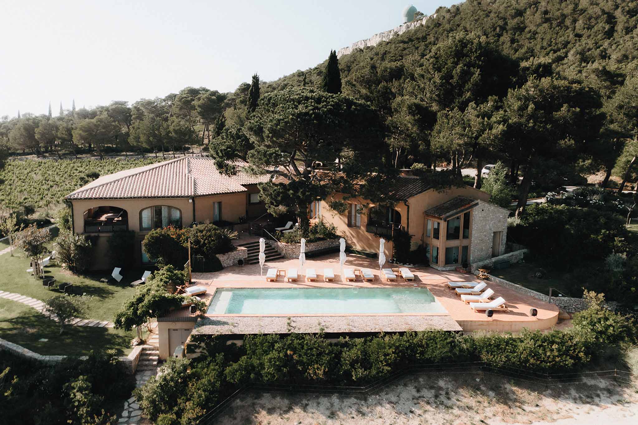 Aerial view of ochre Provencal venue with pool deck, white parasols, arched terrace, and vineyard