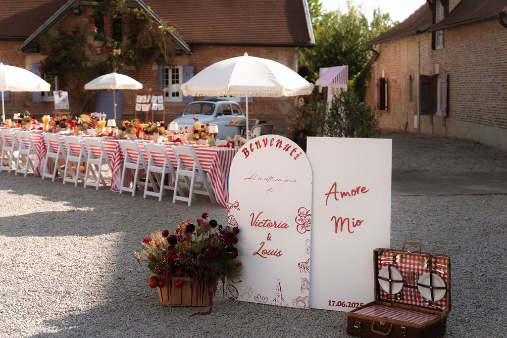 Red and white striped table with dahlia centerpieces and Italian welcome signs at brick farmhouse courtyard