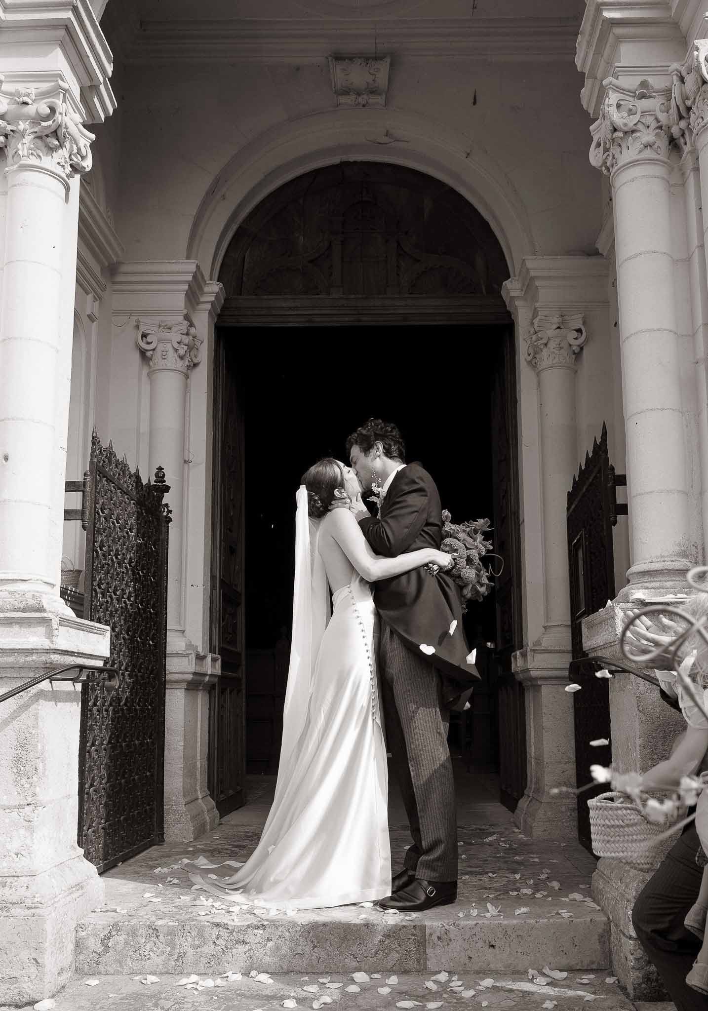 Black and white couple kissing on church steps with scattered petals and Corinthian columns