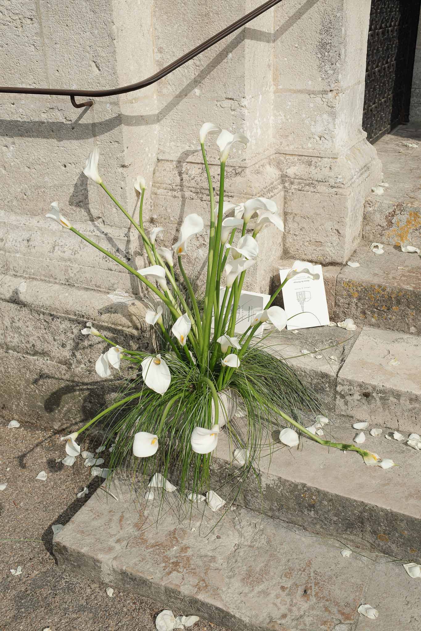 White calla lily arrangement on church steps with scattered petals and ceremony booklet