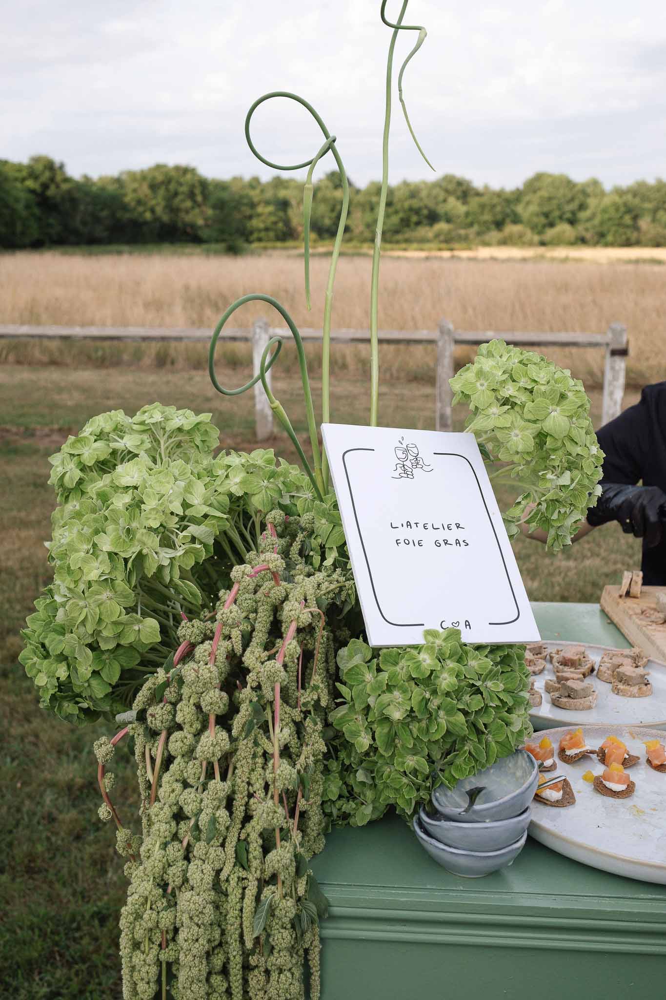 Foie gras tasting station with green hydrangea and amaranthus arrangement on sage table in countryside