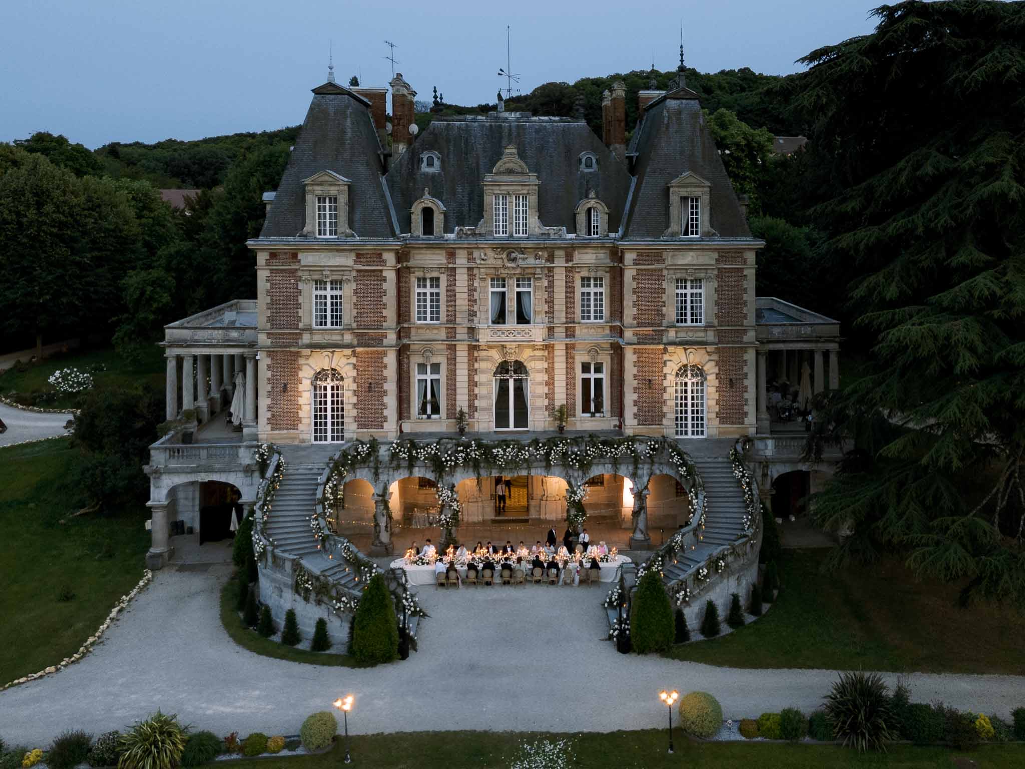 Aerial dusk view of reception dinner at chateau staircase decorated with white roses and greenery