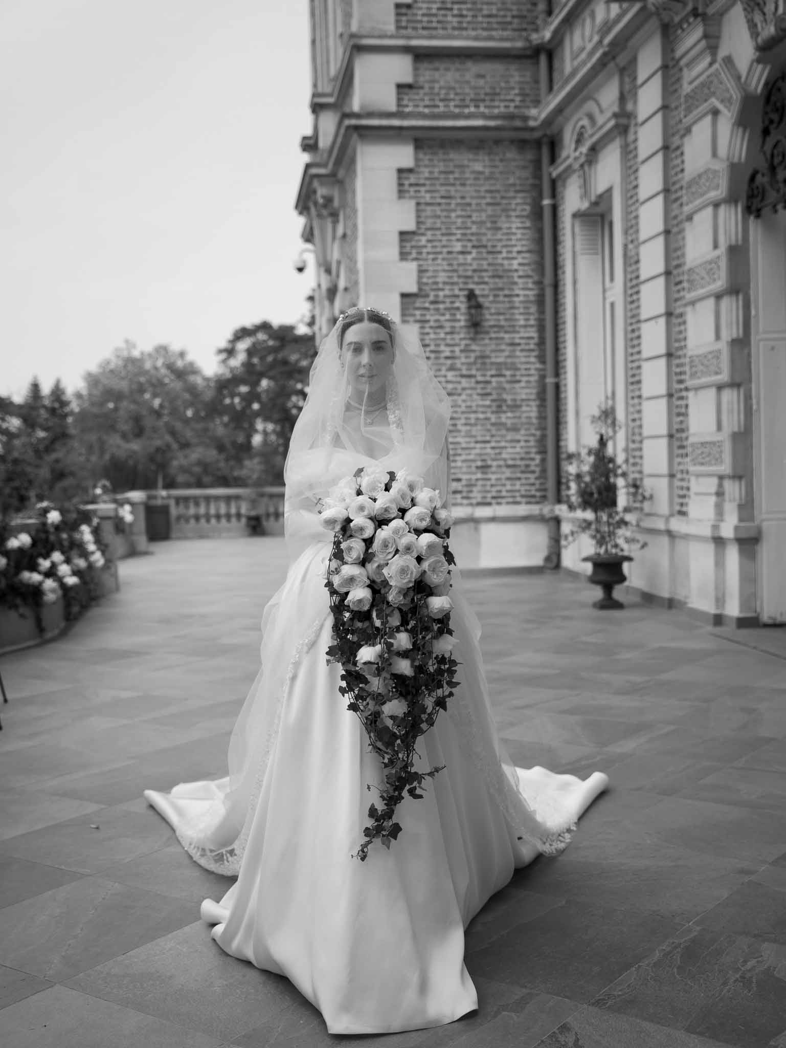 Black and white bride with cathedral train and cascading rose bouquet on stone terrace of brick and stone chateau