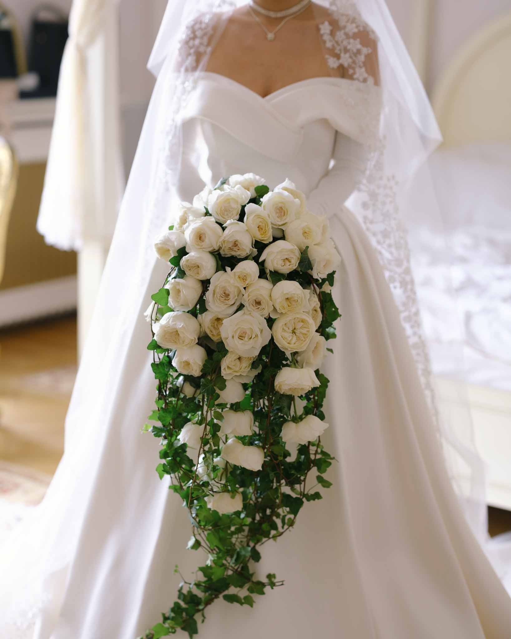 Bride in off-shoulder satin ballgown holding cascading ivory rose and ivy teardrop bouquet
