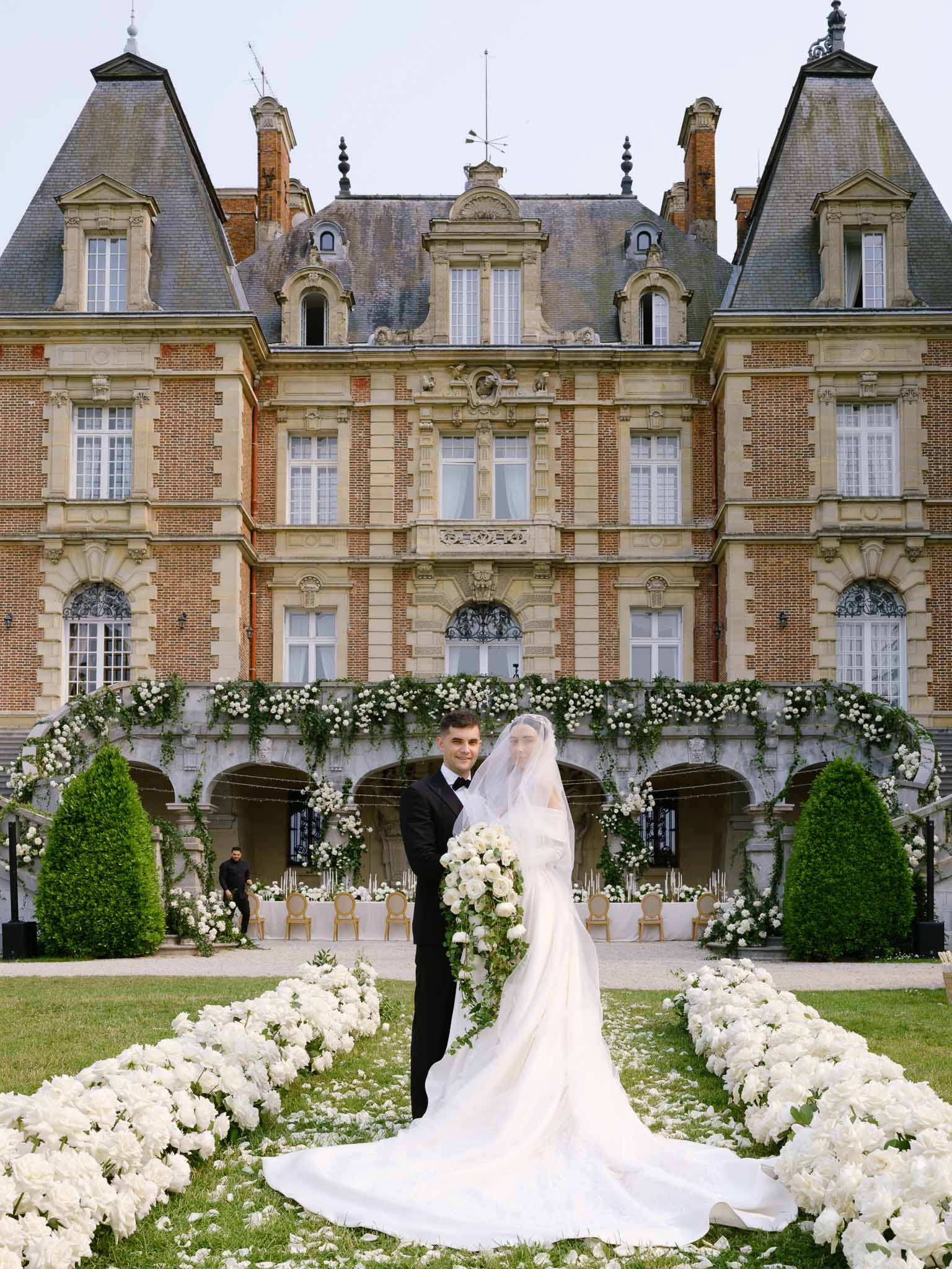 Couple at end of white rose aisle before grand chateau with floral garland loggia bride in ballgown with cathedral veil