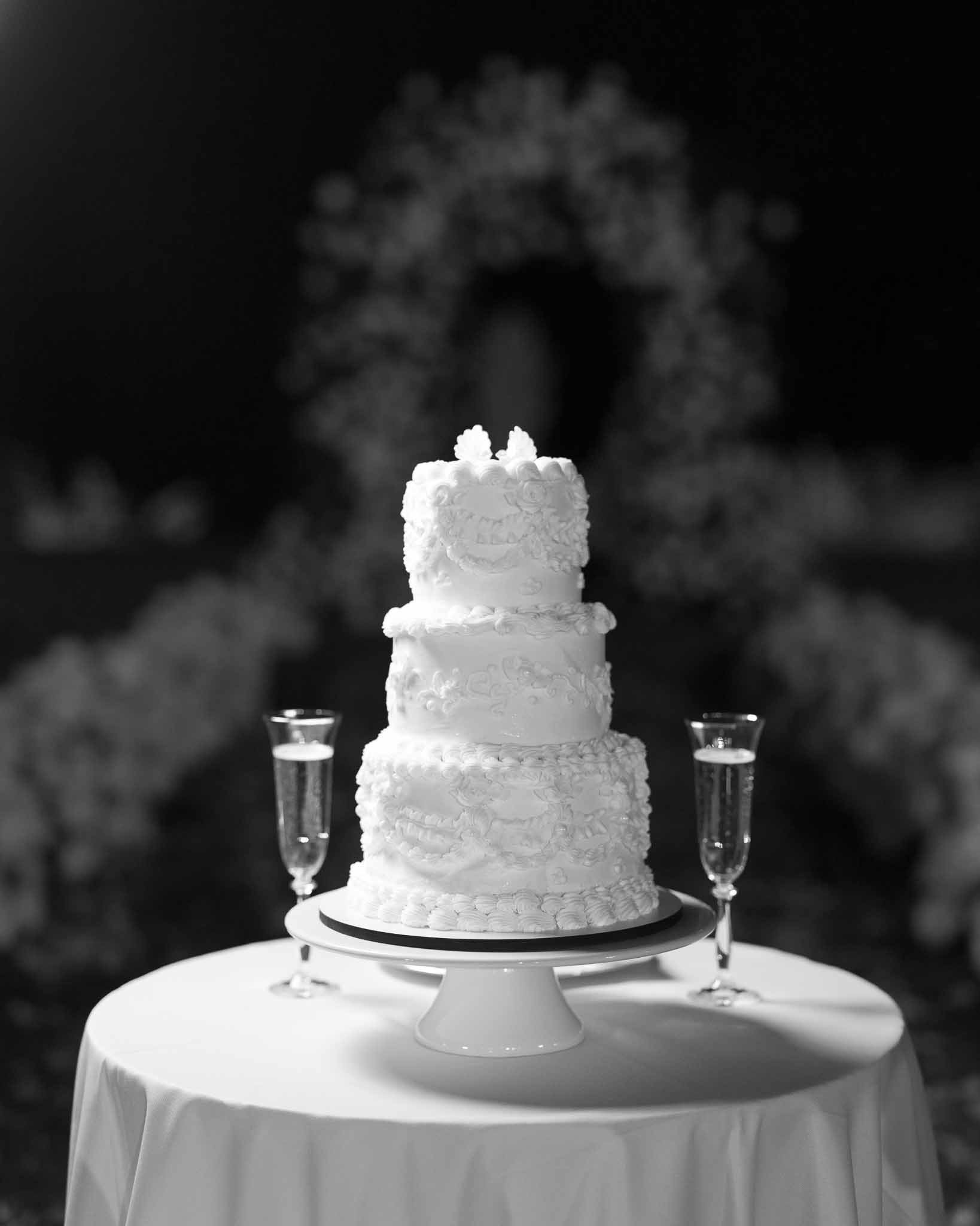 Black-and-white three-tier ruffled wedding cake on white pedestal stand flanked by two champagne flutes