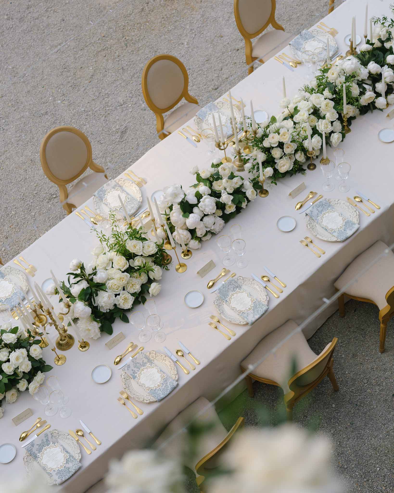 Aerial view of feasting table with white rose runner, gold candelabras, and blue toile charger plates