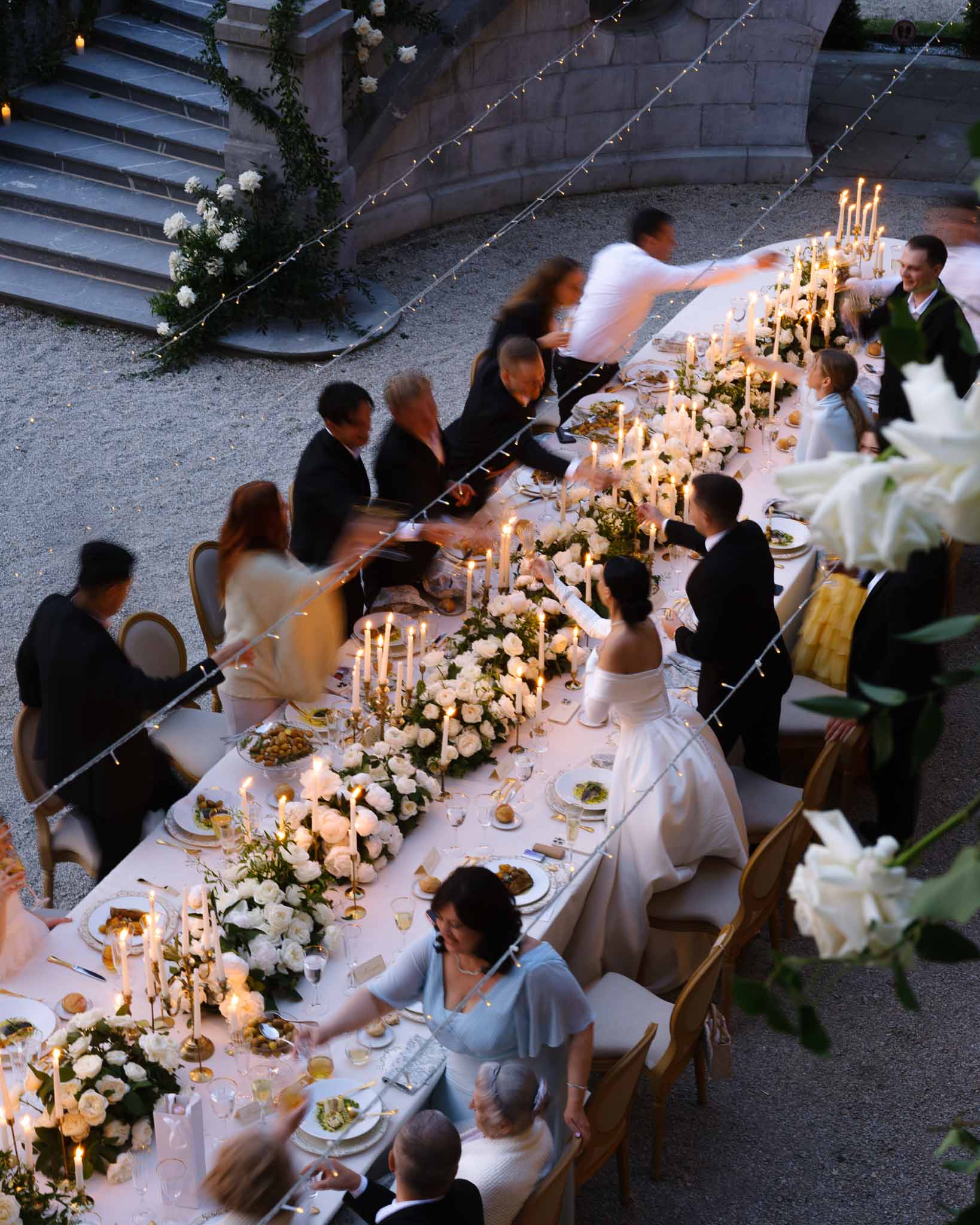 Aerial dusk reception with bride toasting at white rose runner banquet table with brass candles