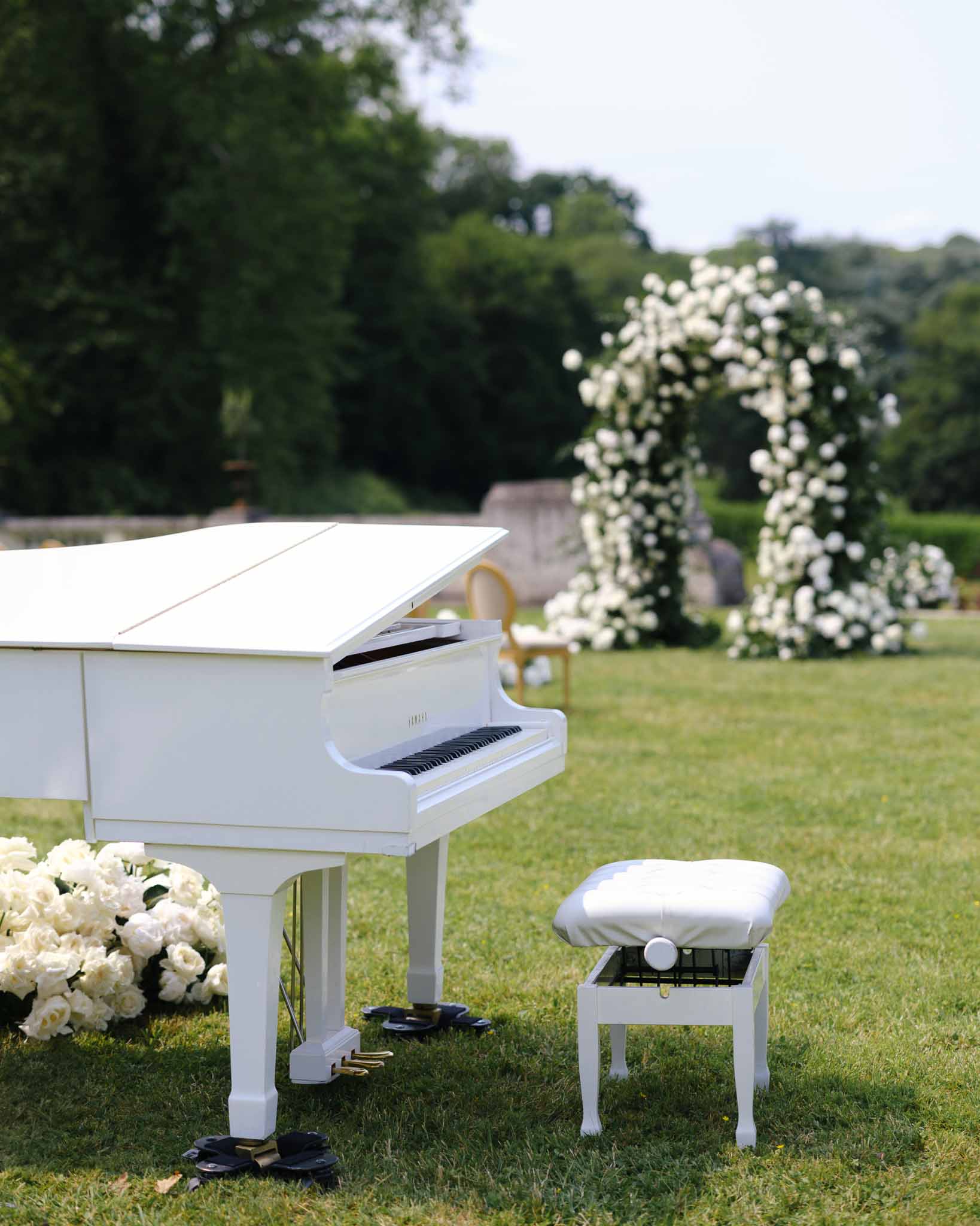 White baby grand piano with ivory rose cluster before circular white rose ceremony arch on lawn