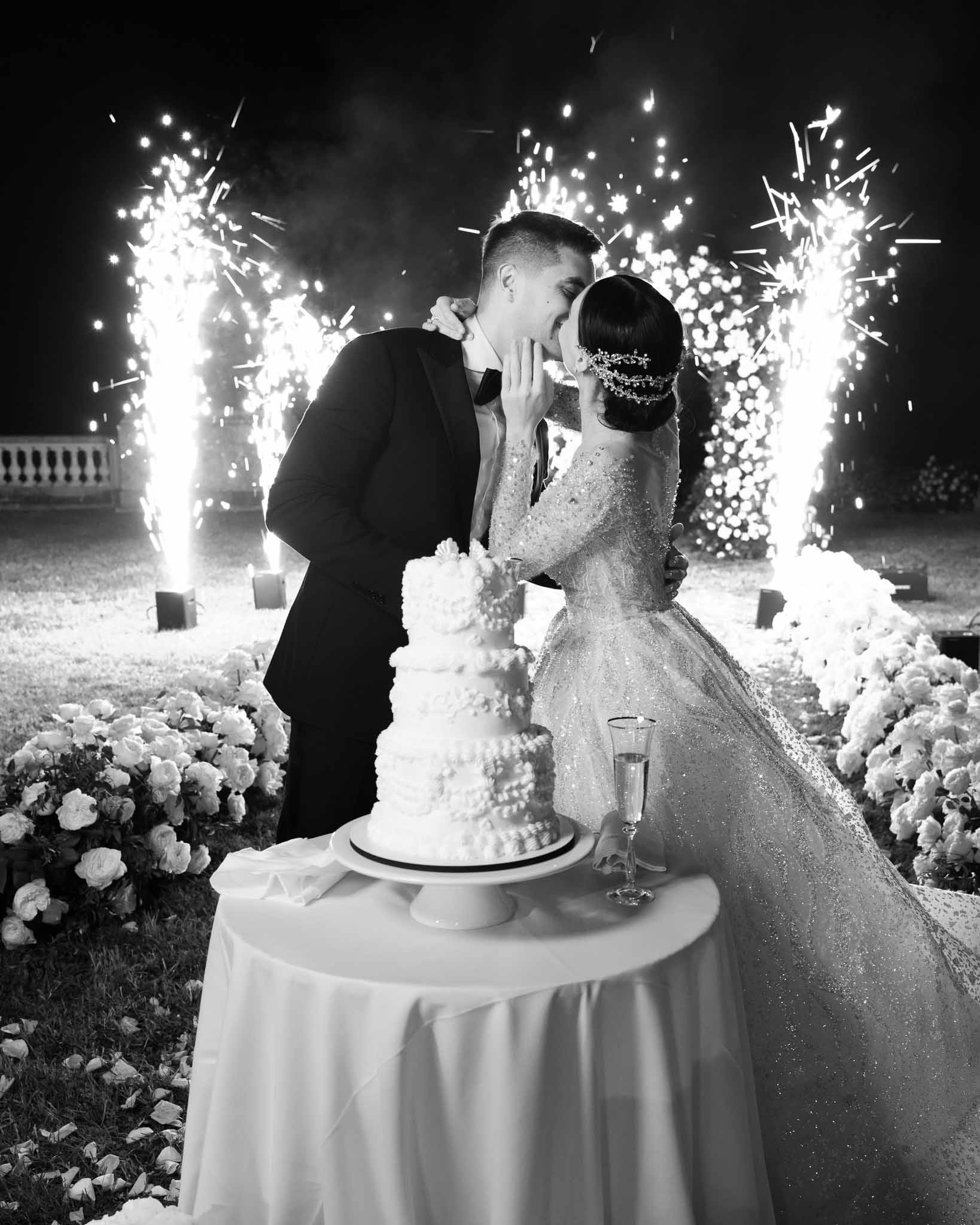 Black and white couple kissing over four-tier cake with cold sparkler fountains and white rose ground installations