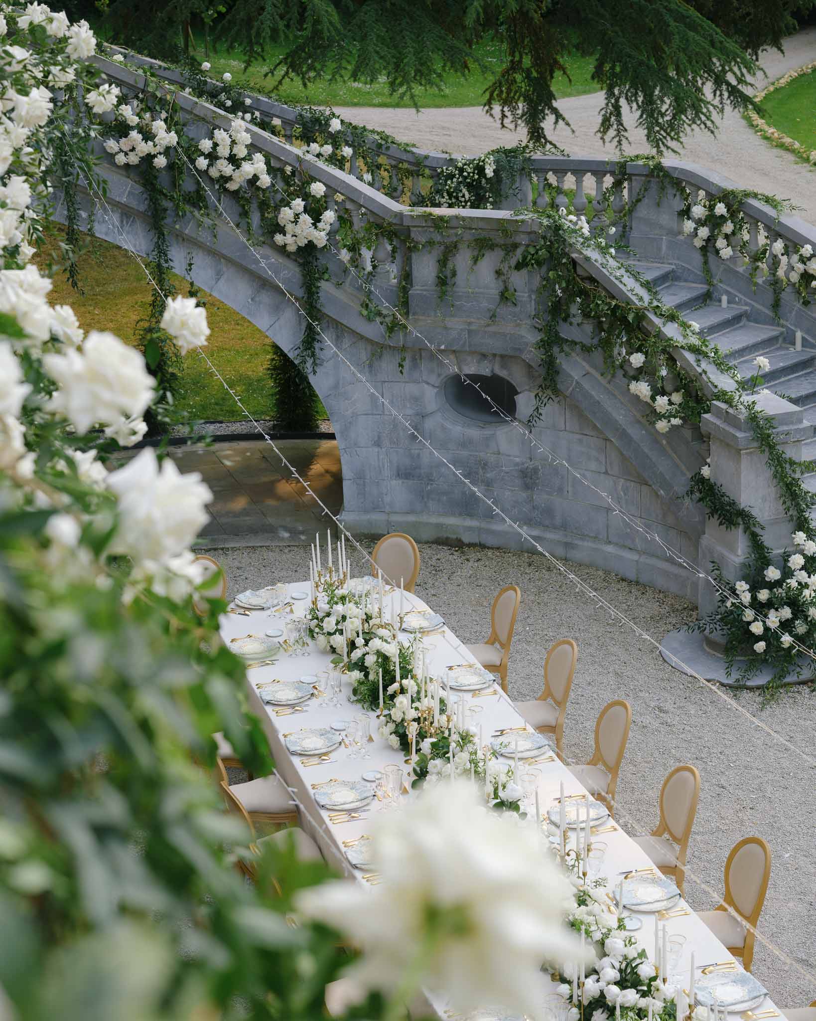 Elevated view of reception table with white rose runner, gold cutlery, and blue patterned plates at stone staircase