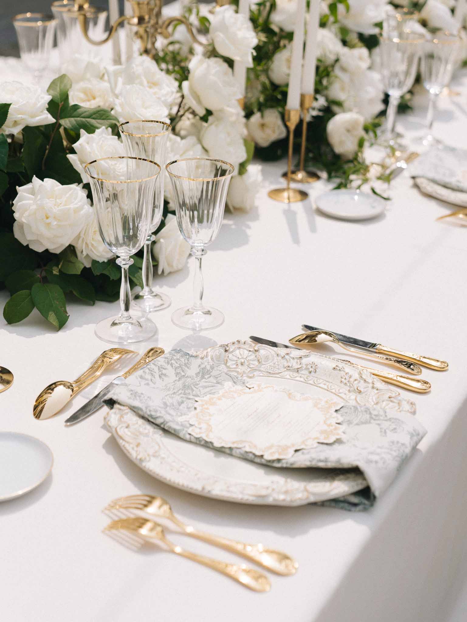 Place setting with embossed charger, sage damask napkin, gold flatware, and white rose runner with taper candles