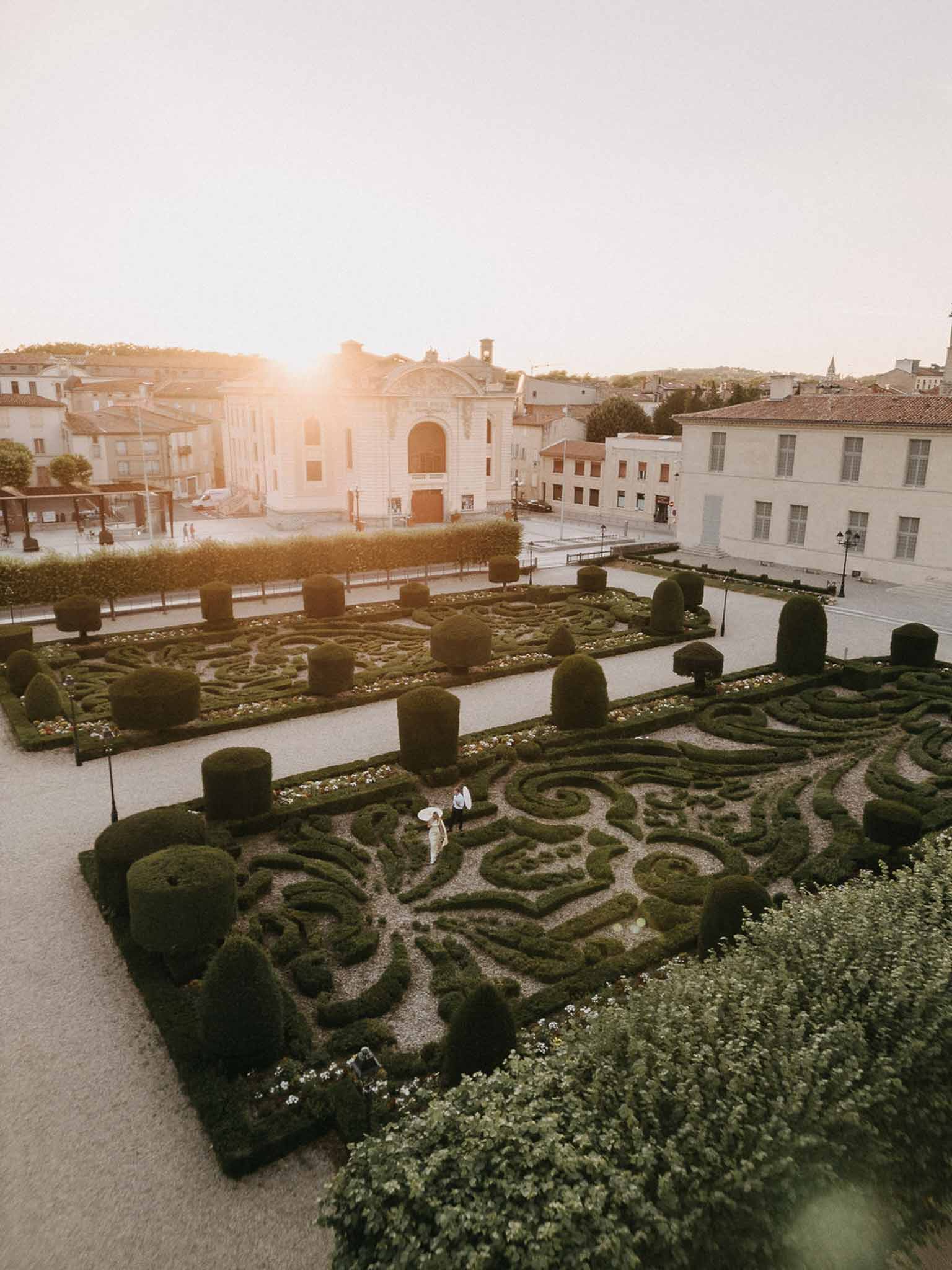 Aerial view of couple walking through formal French parterre garden at golden hour with geometric topiary