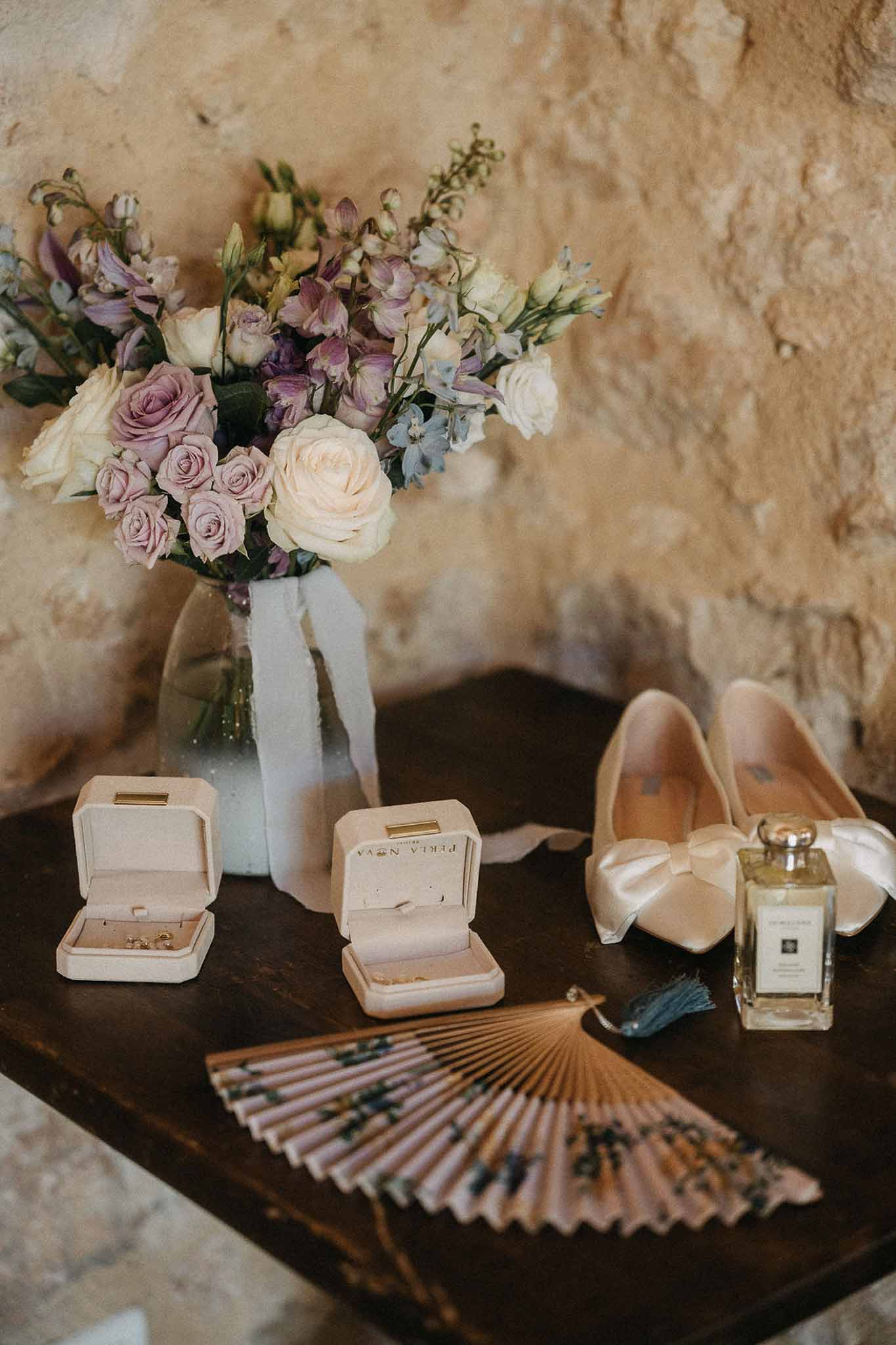 Bridal flat lay with mauve rose bouquet, blush velvet ring boxes, satin bow shoes, and Jo Malone perfume