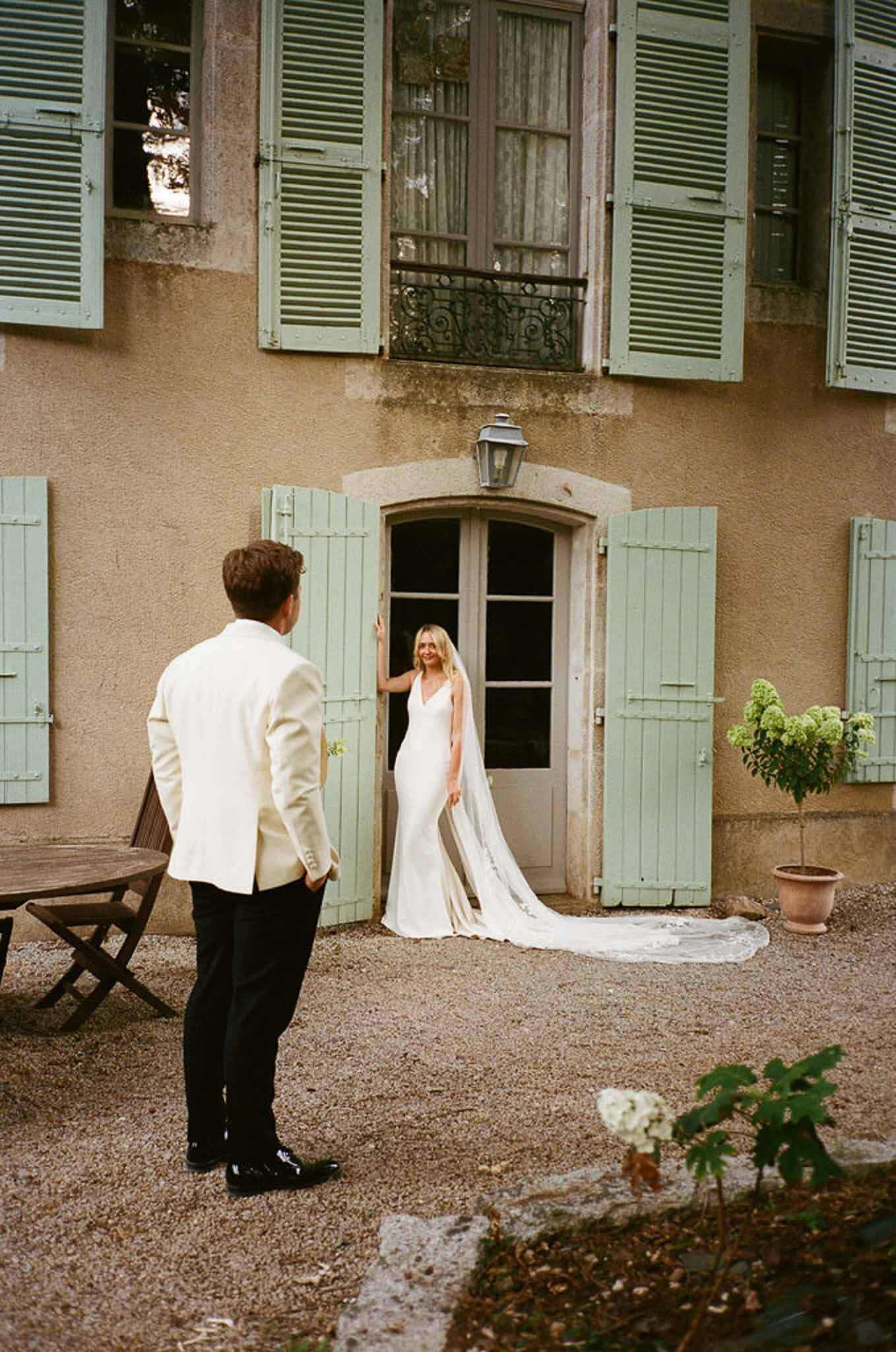 Groom facing bride in arched doorway of Provencal mas with sage green shutters during first look moment