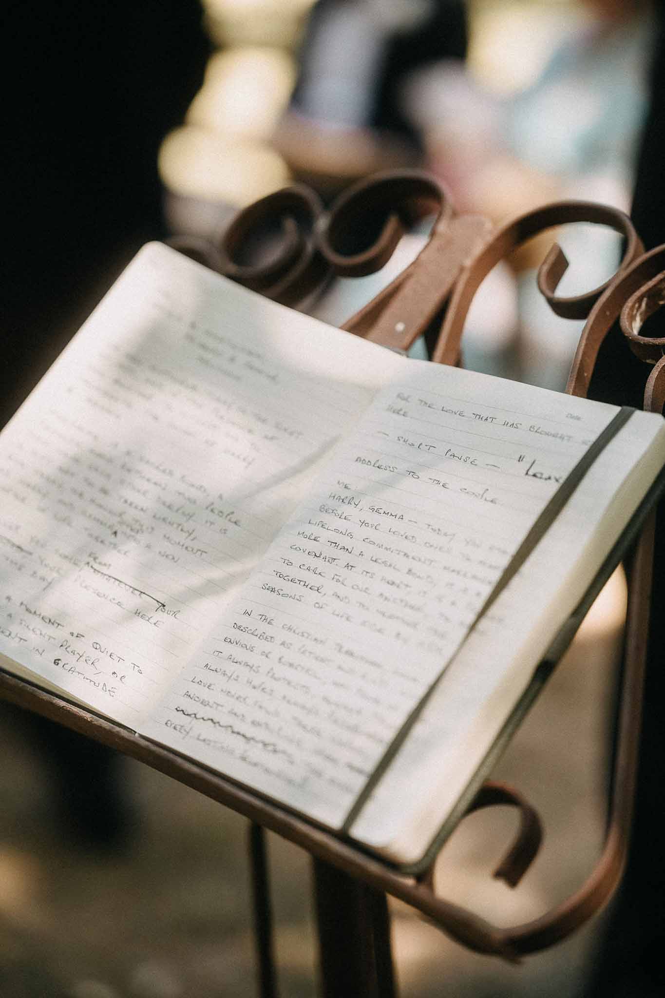 Open notebook on wrought-iron lectern with handwritten ceremony vows and warm golden bokeh background