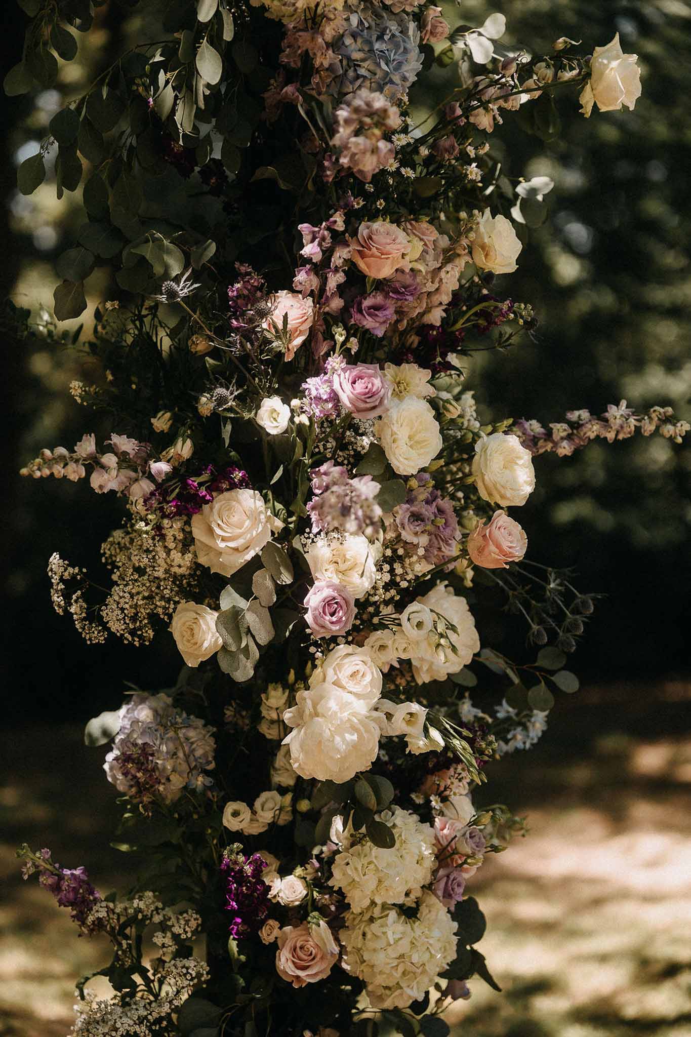 Close-up of ceremony arch with ivory peonies, blush roses, mauve blooms, eryngium, and eucalyptus